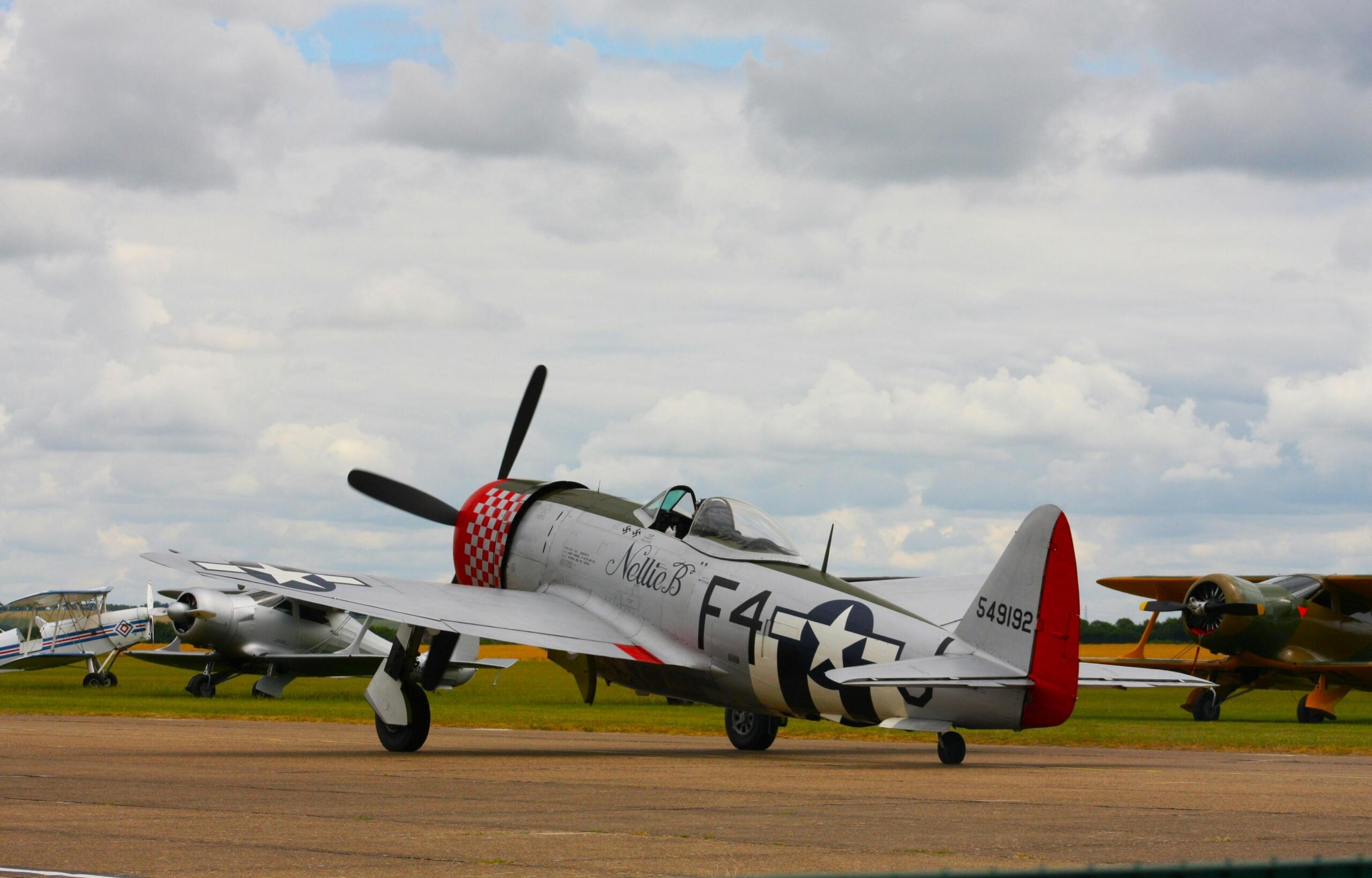 A P-47 Thunderbolt fighter on a runway beneath a cloudy sky.