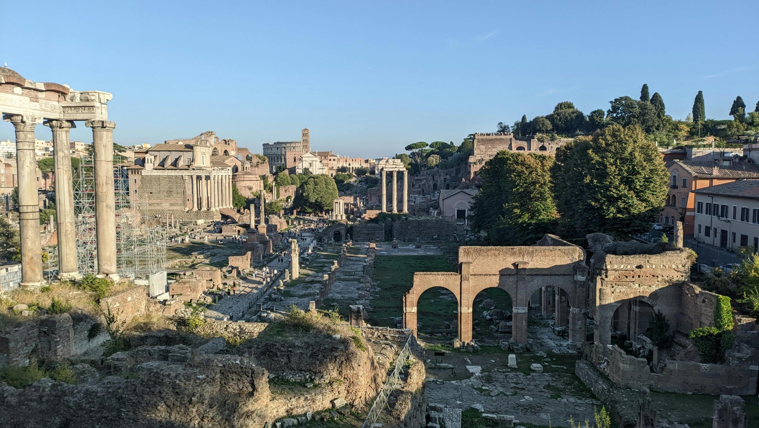 Ruins of the Roman Forum with weathered columns and arches among ancient stone under a blue sky.