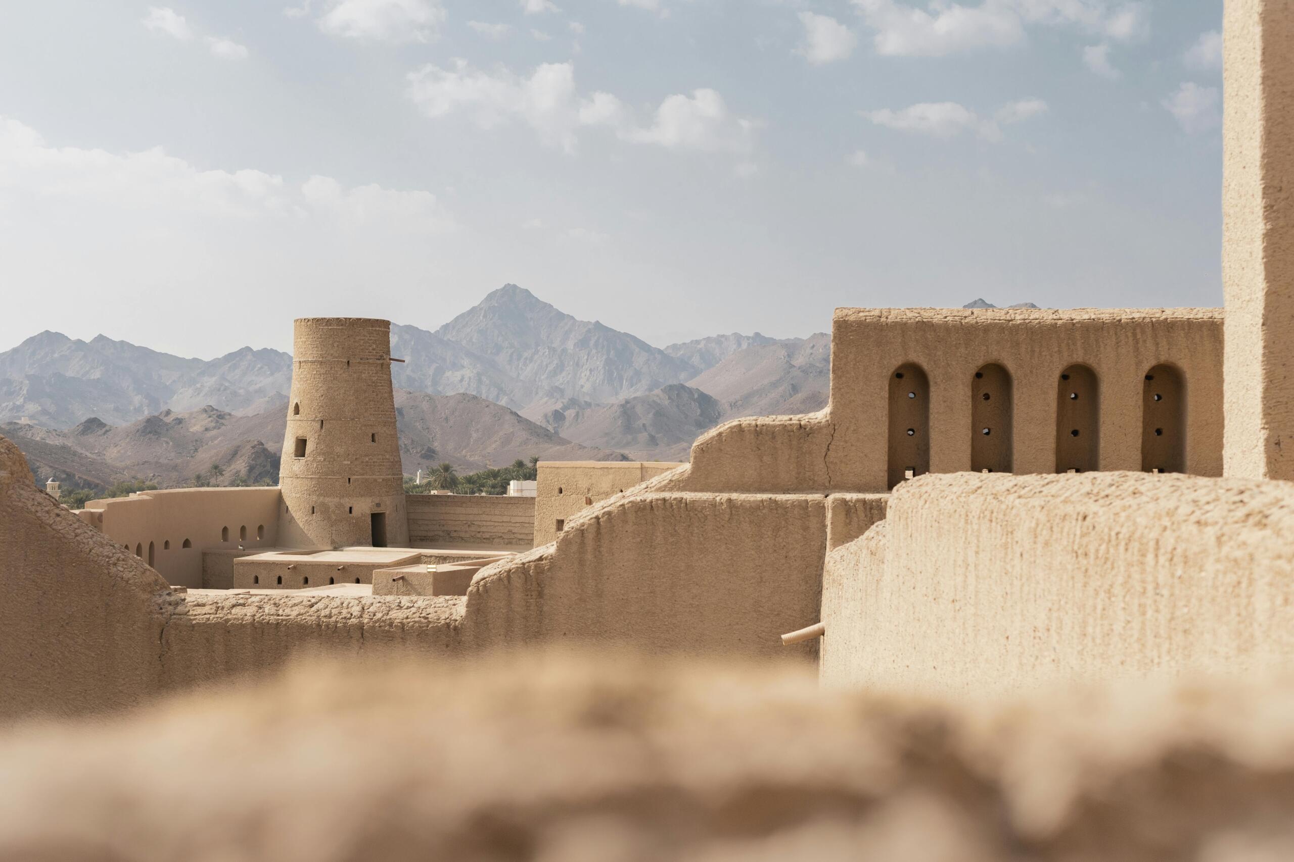 Sand-coloured fortress with a round tower and desert-like mountains in the background.