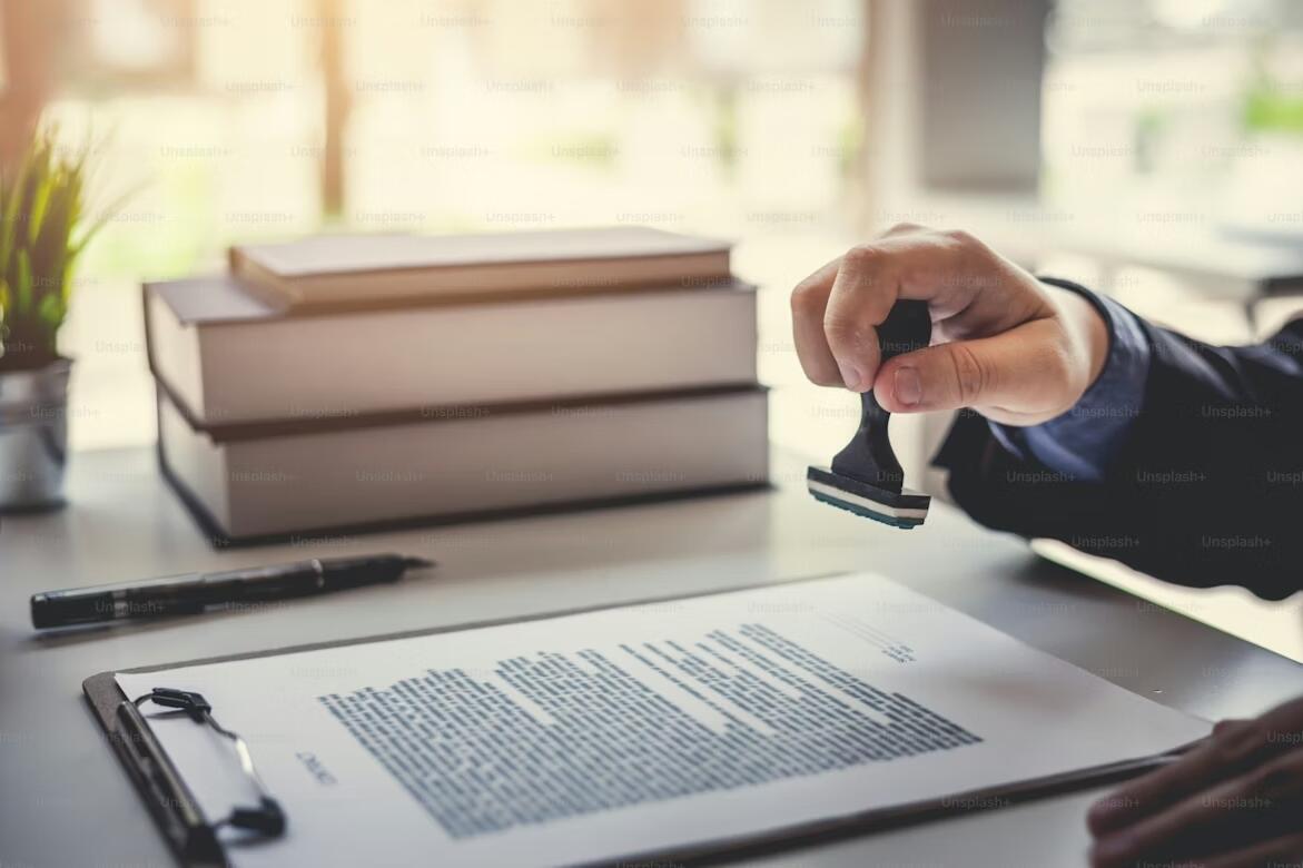 Close-up of a hand stamping an official document on a clipboard, with a stack of books in the background, symbolizing French exam certification approval.