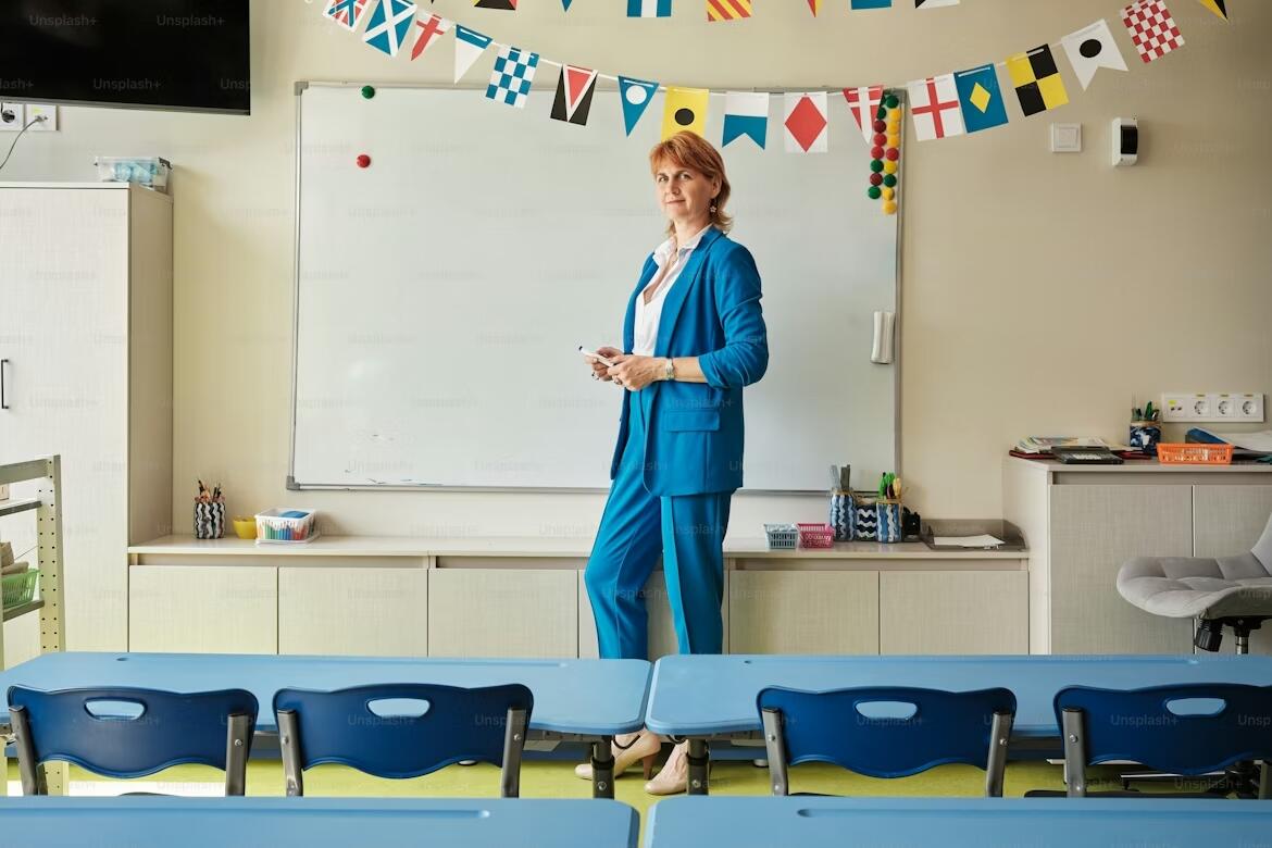 A language teacher standing in front of a whiteboard in a bright classroom decorated with international flags, holding a marker and preparing to teach a lesson.