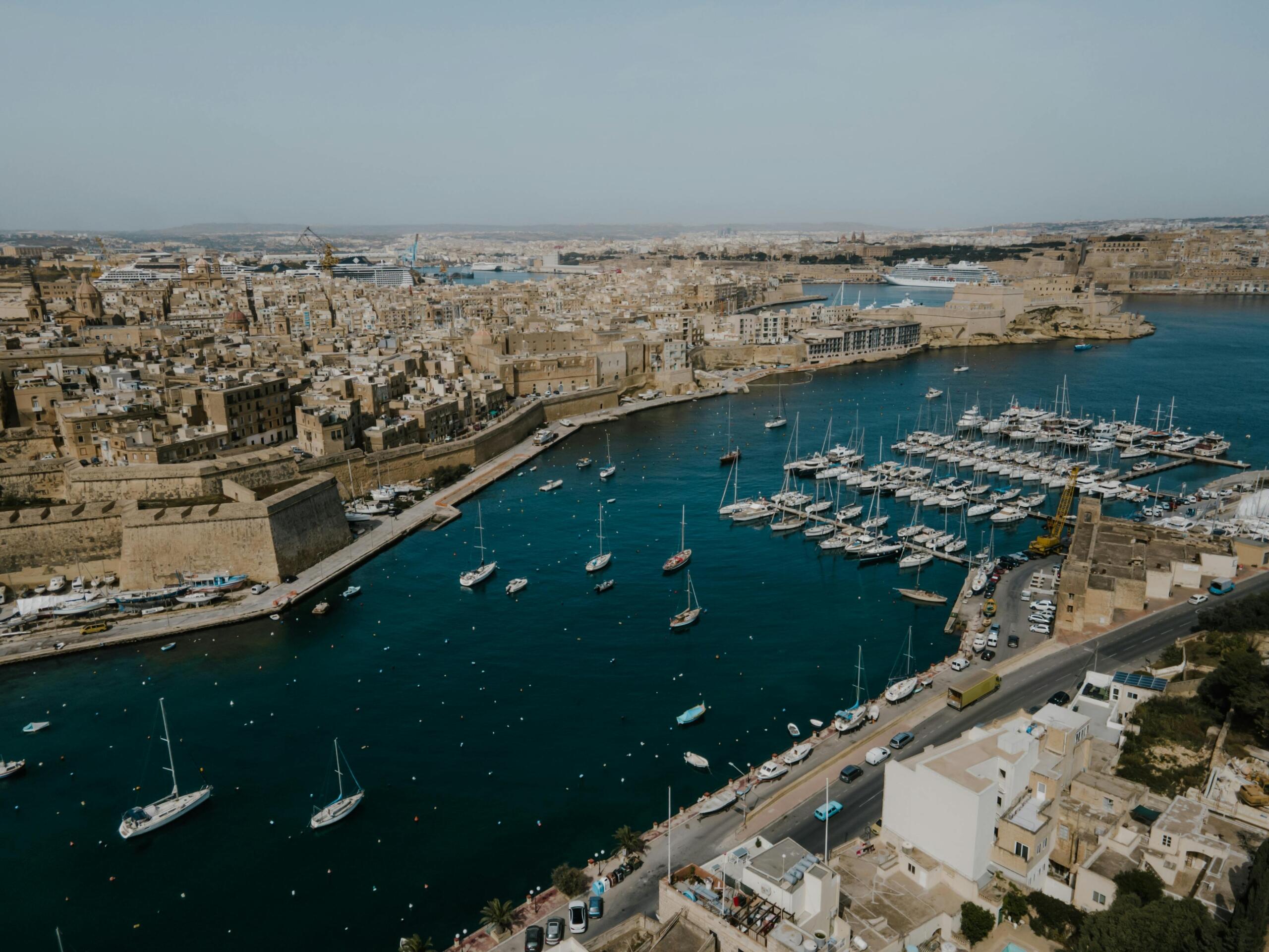 Aerial view of a harbour with yachts and historic city buildings around deep blue water.