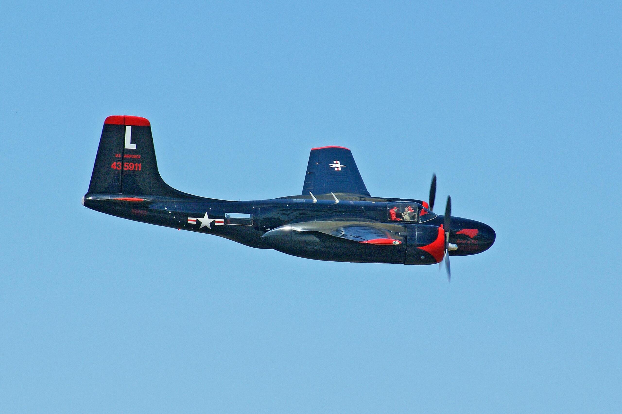 Dark blue B-26 Invader aircraft with red accents flying across a cloudless sky.