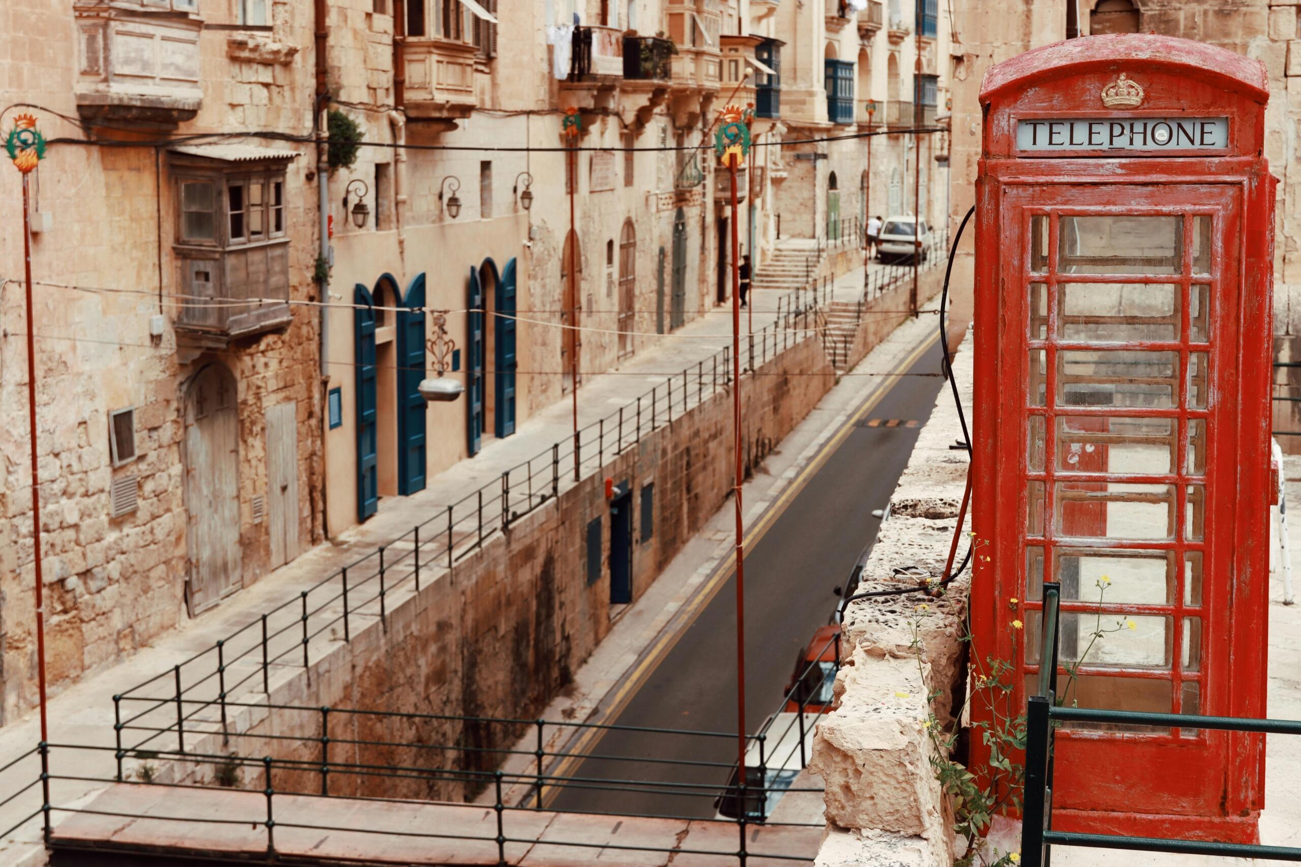 Red British telephone box standing in a street with limestone houses in Valletta.