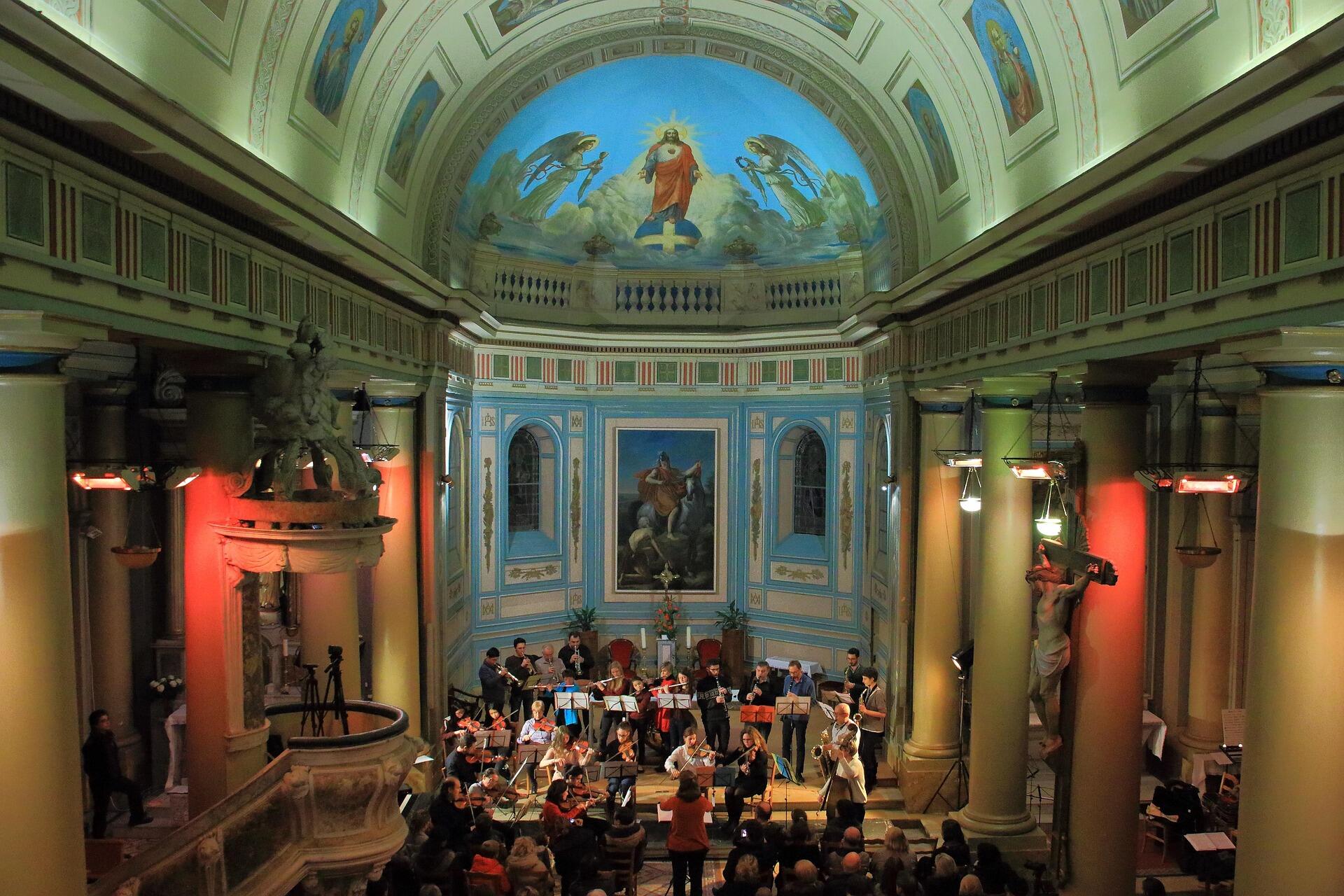 Orchestra performing Easter sacred music concert inside a historic church with frescoed dome and crucifix statue