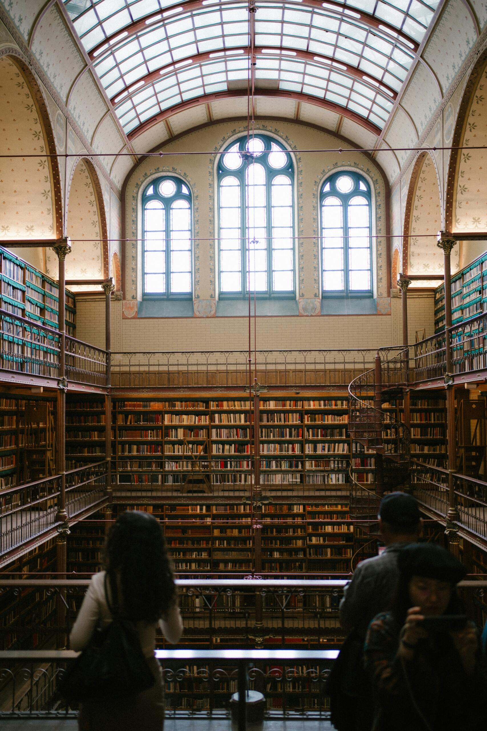 A grand library interior with rows of tall bookshelves and arched windows, filled with books under warm lighting.