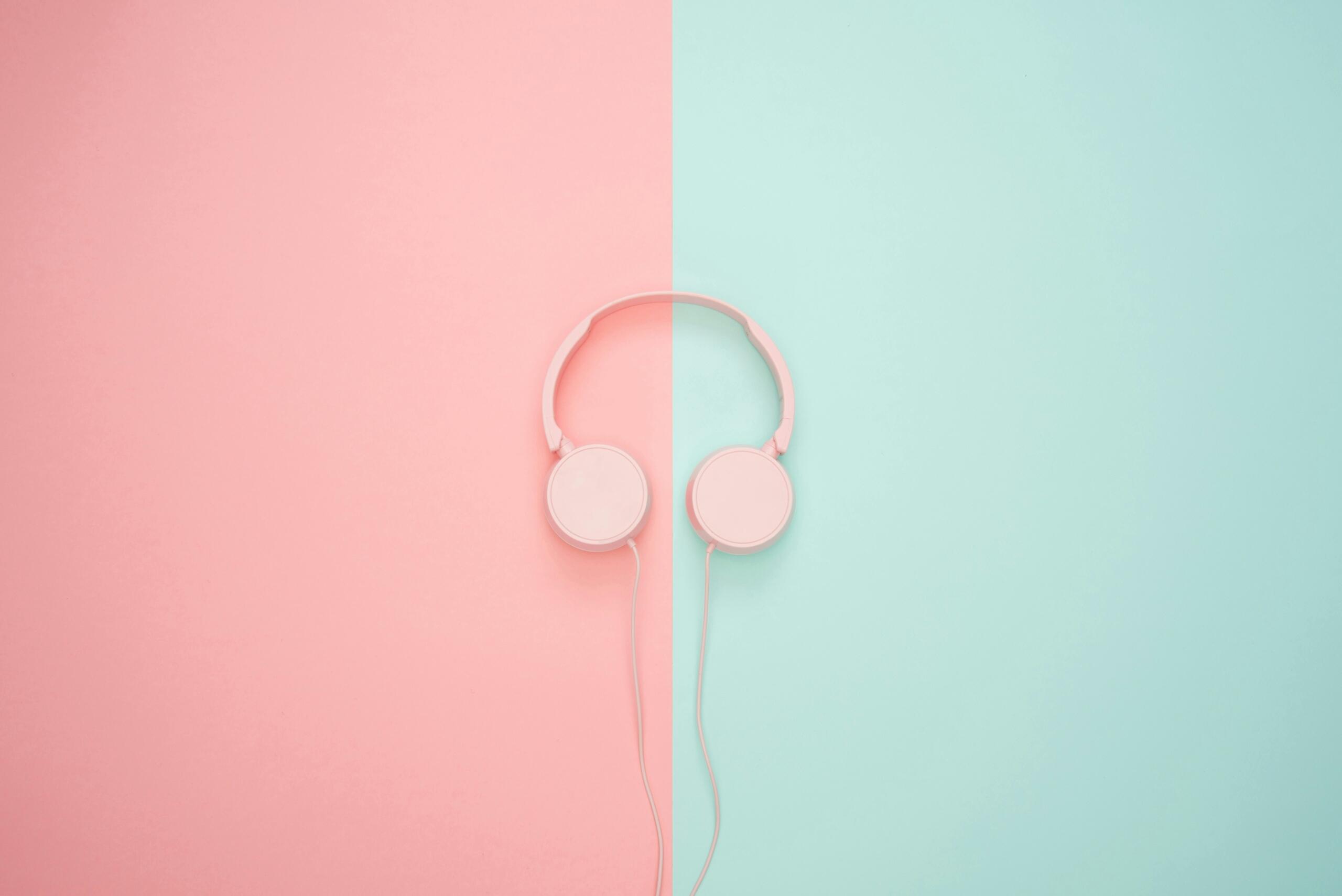 A pair of white corded headphones lies on a flat surface divided into pastel pink and turquoise halves.
