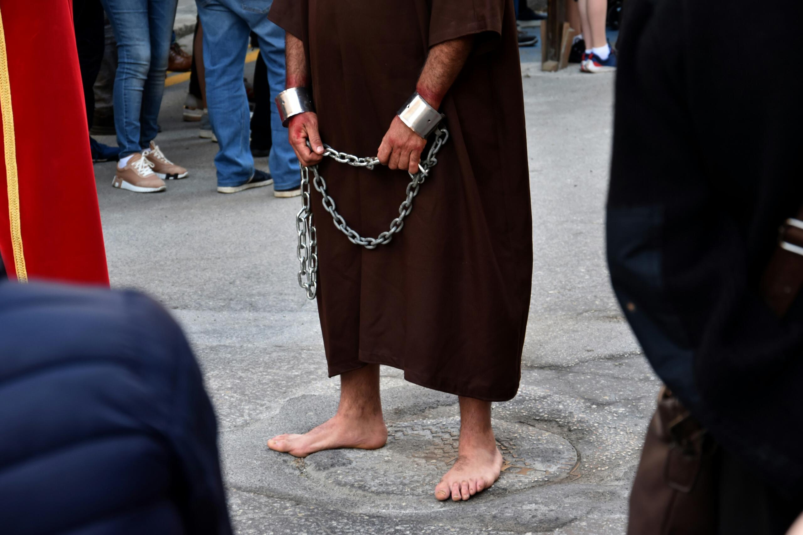 Man in a brown robe and shackles walking barefoot during a Good Friday procession in Malta