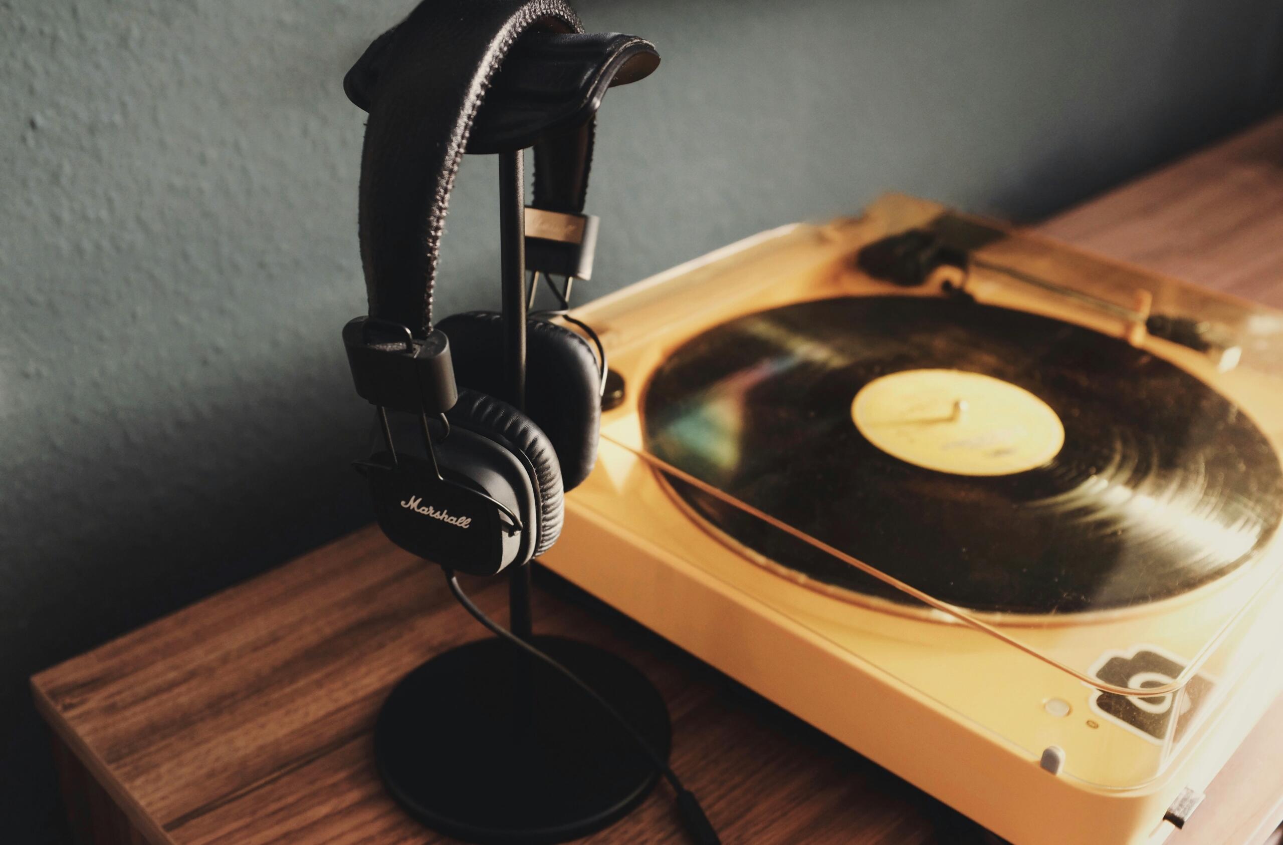 A pair of black Marshall headphones on a stand beside a vintage vinyl record player on a wooden table.