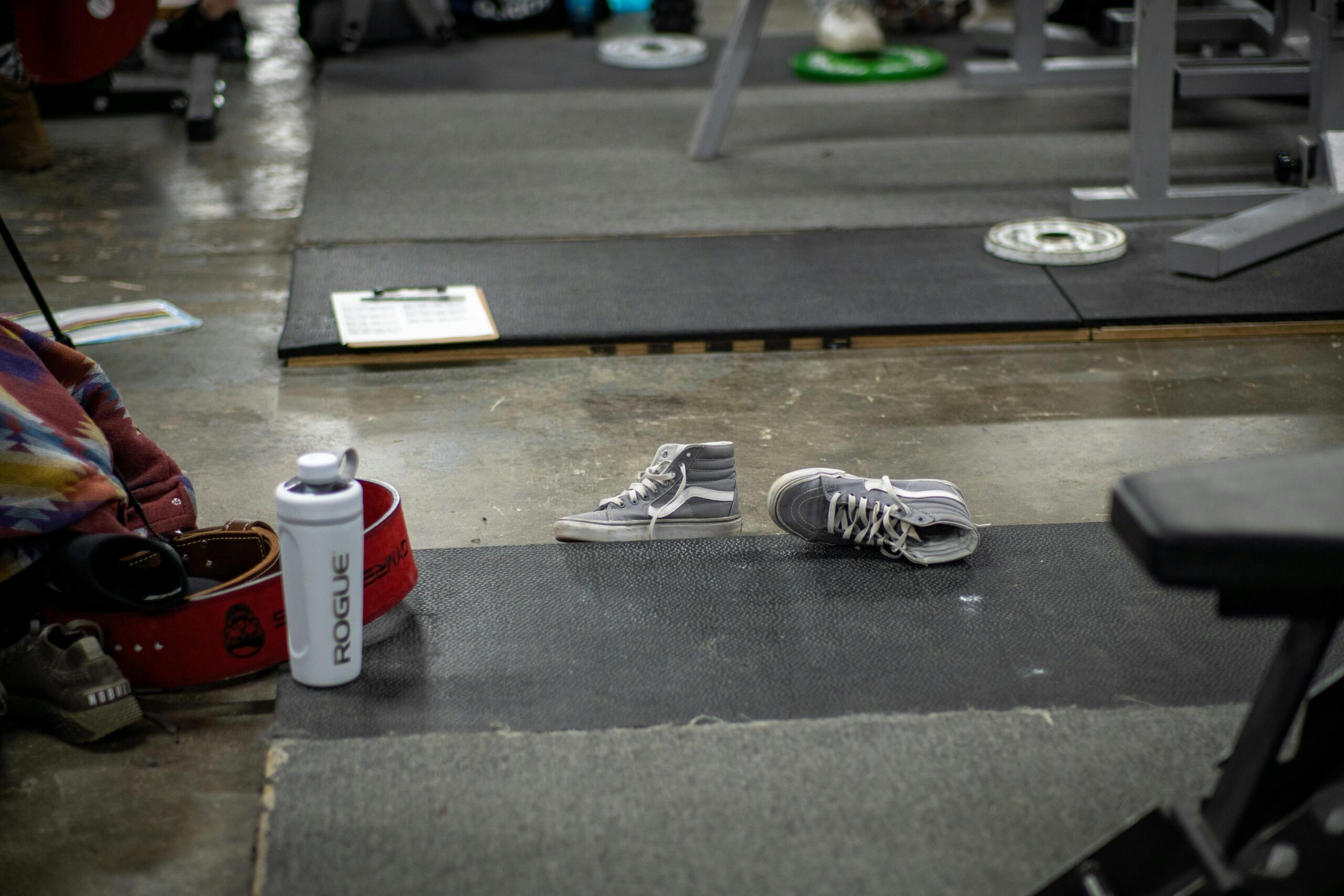 A pair of training shoes sits on a gym floor beside workout equipment.