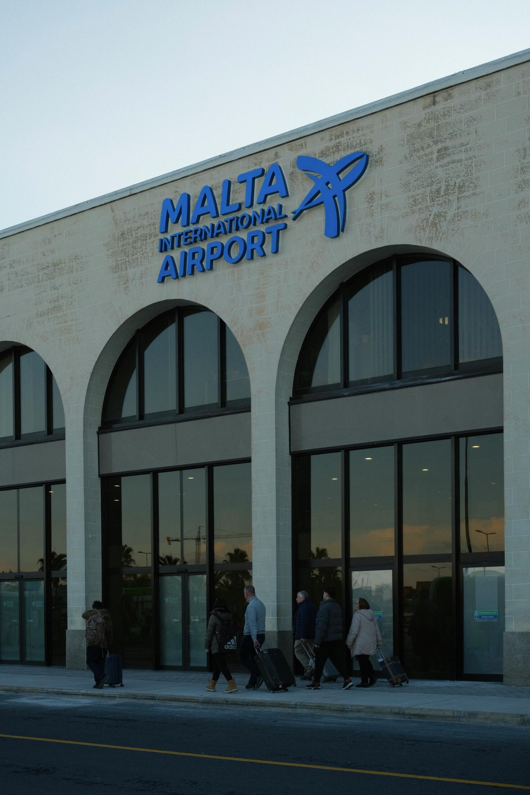 People walk with luggage outside the entrance of Malta International Airport.
