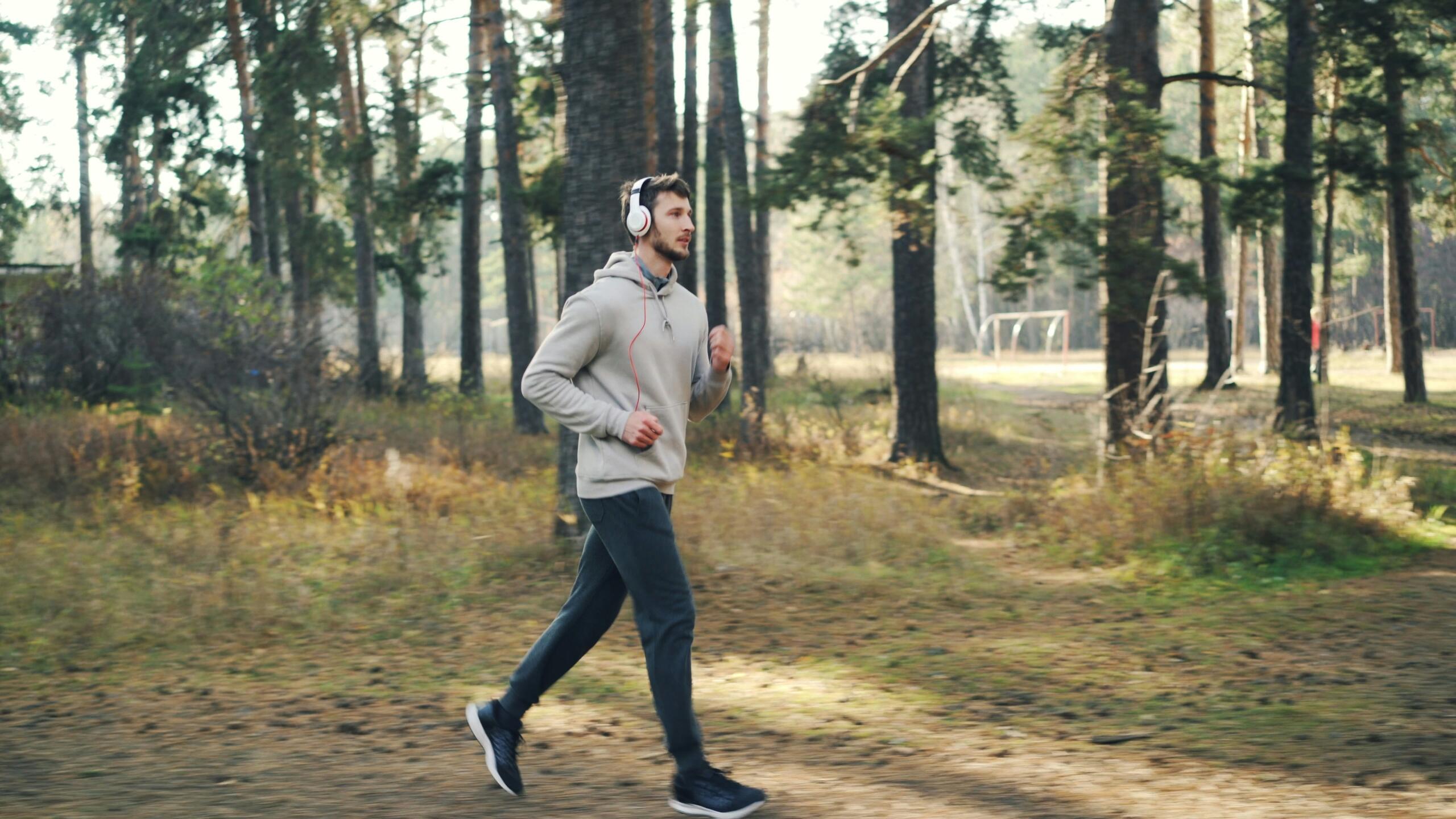 A man runs through a forest trail while wearing headphones and sportswear.