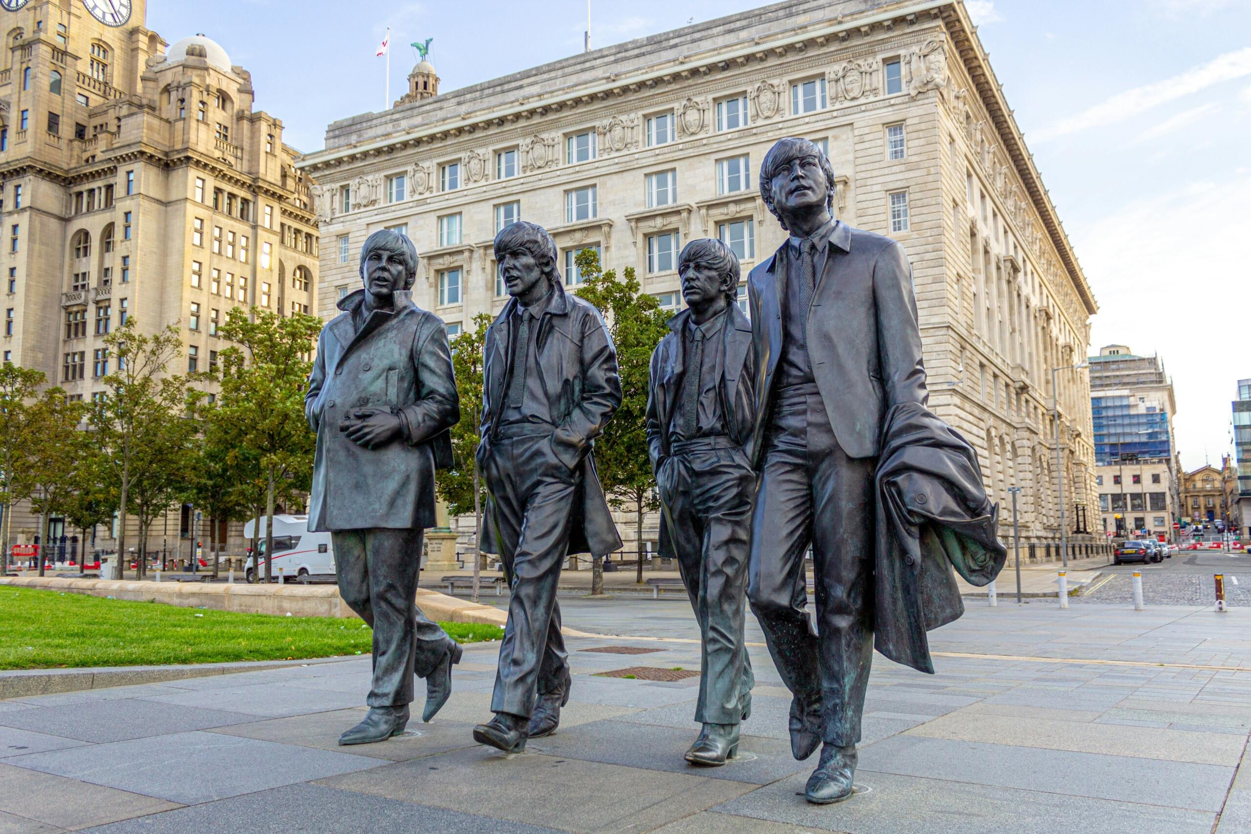 four dark statues in daylight in front of a big bright building