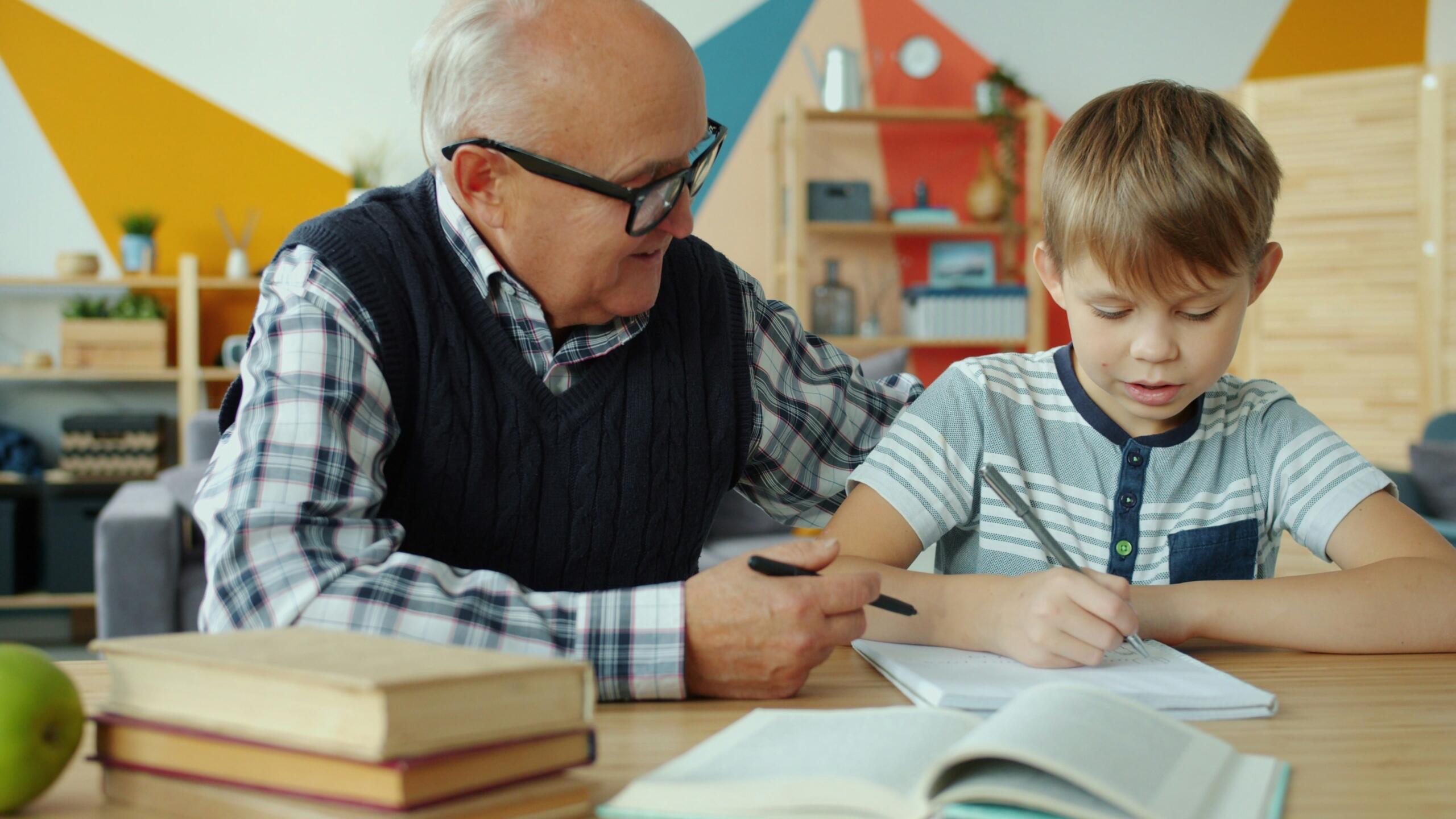 An older man helps a young boy with homework at a desk.