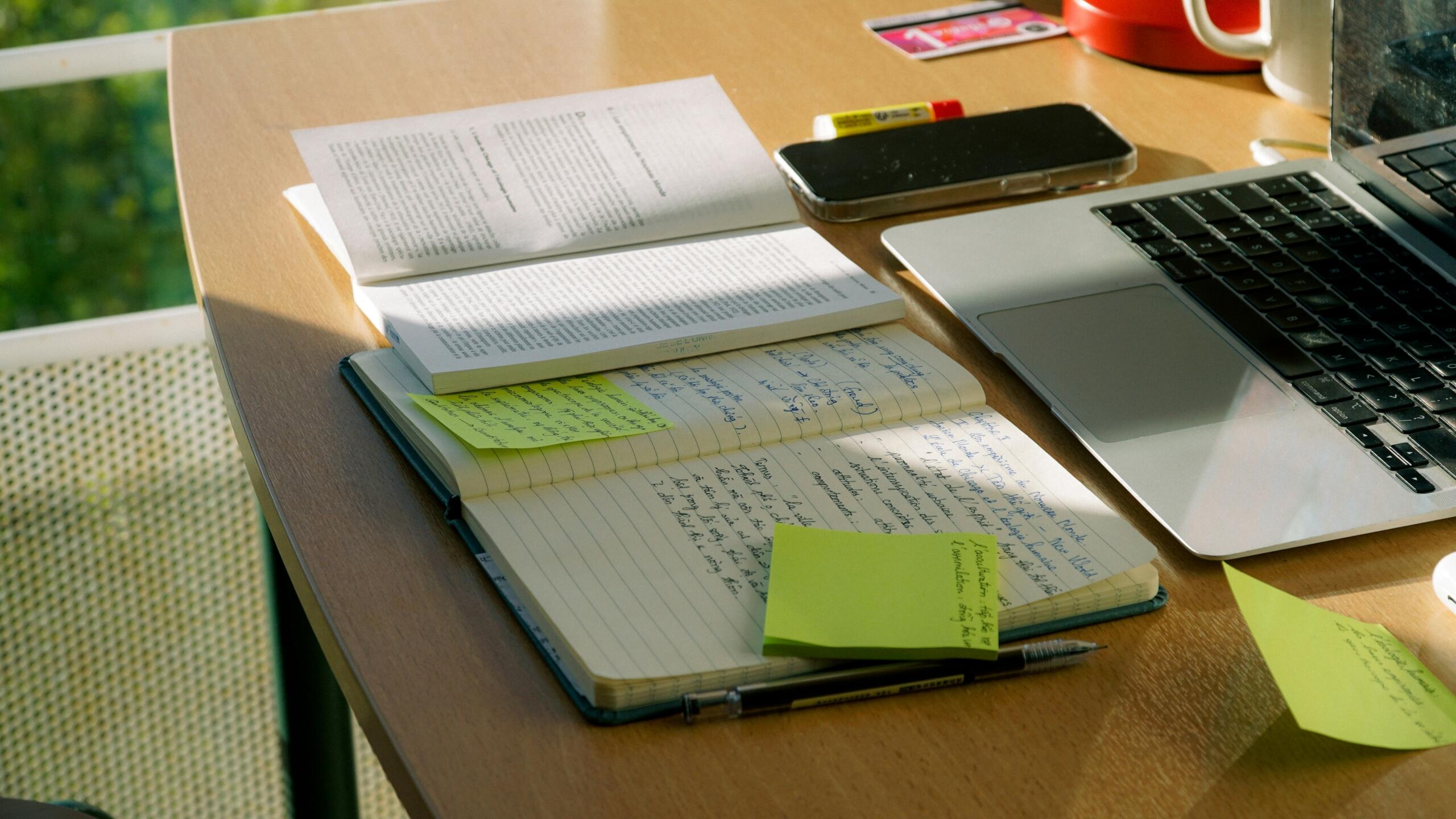 A laptop and notebook sit on a work desk.
