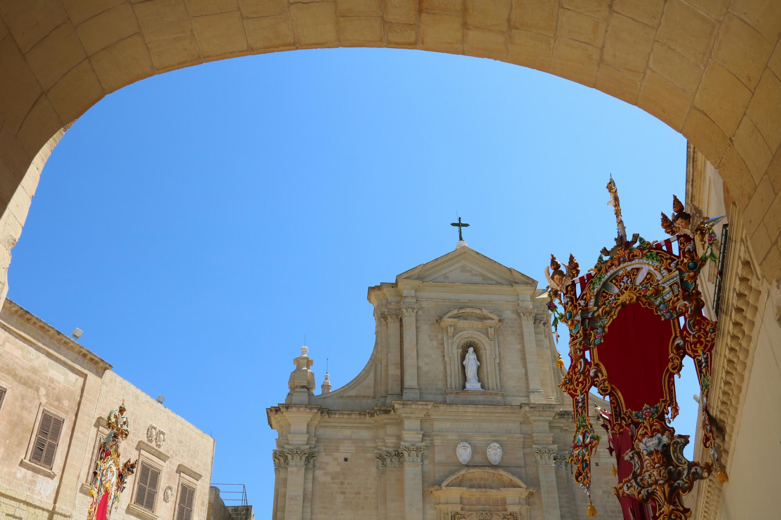 Maltese parish church framed through an arch with ornate festa decorations