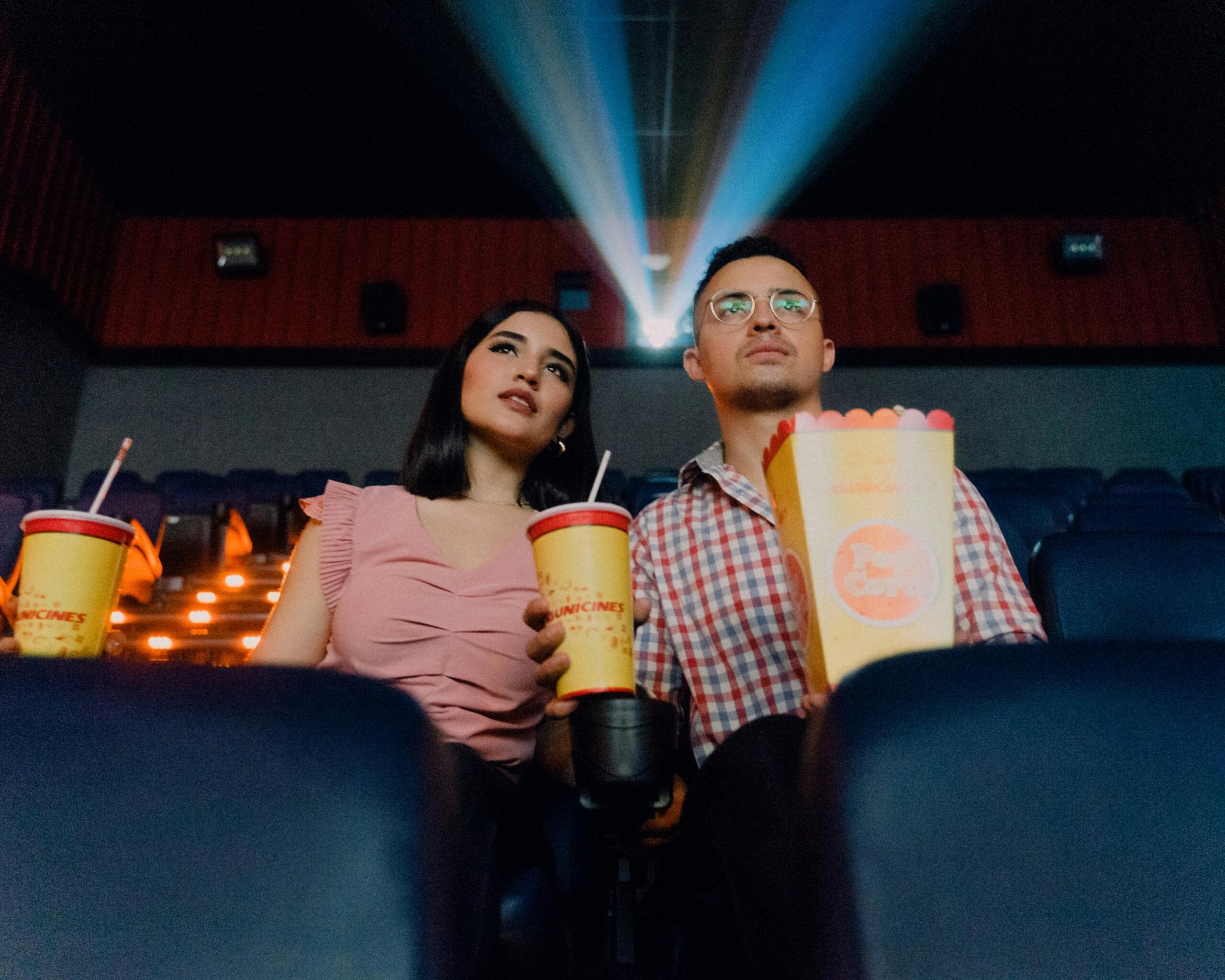 a man and a woman with snacks and drinks watching a movie in a cinema