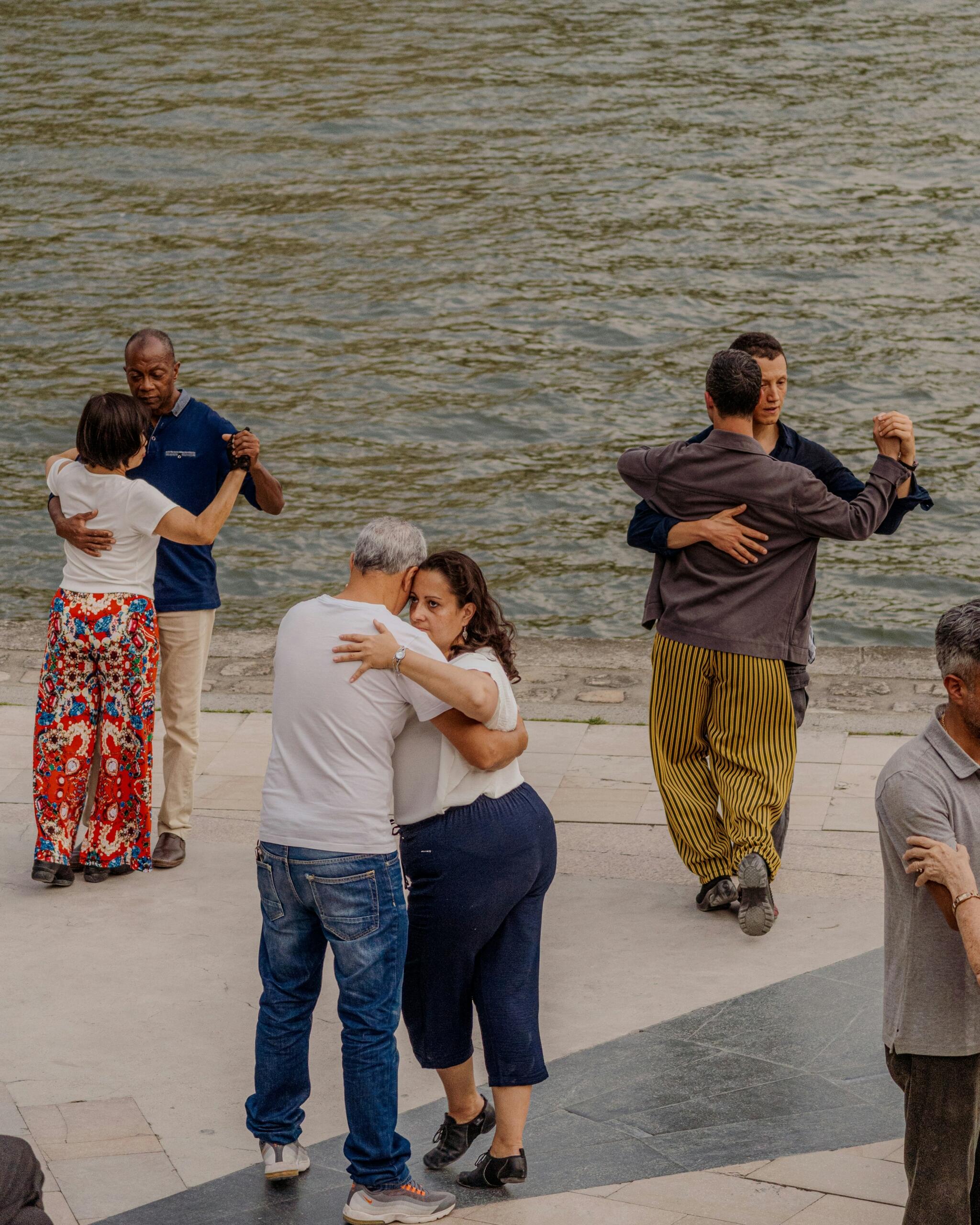 Several couples dance outdoors beside a body of water.