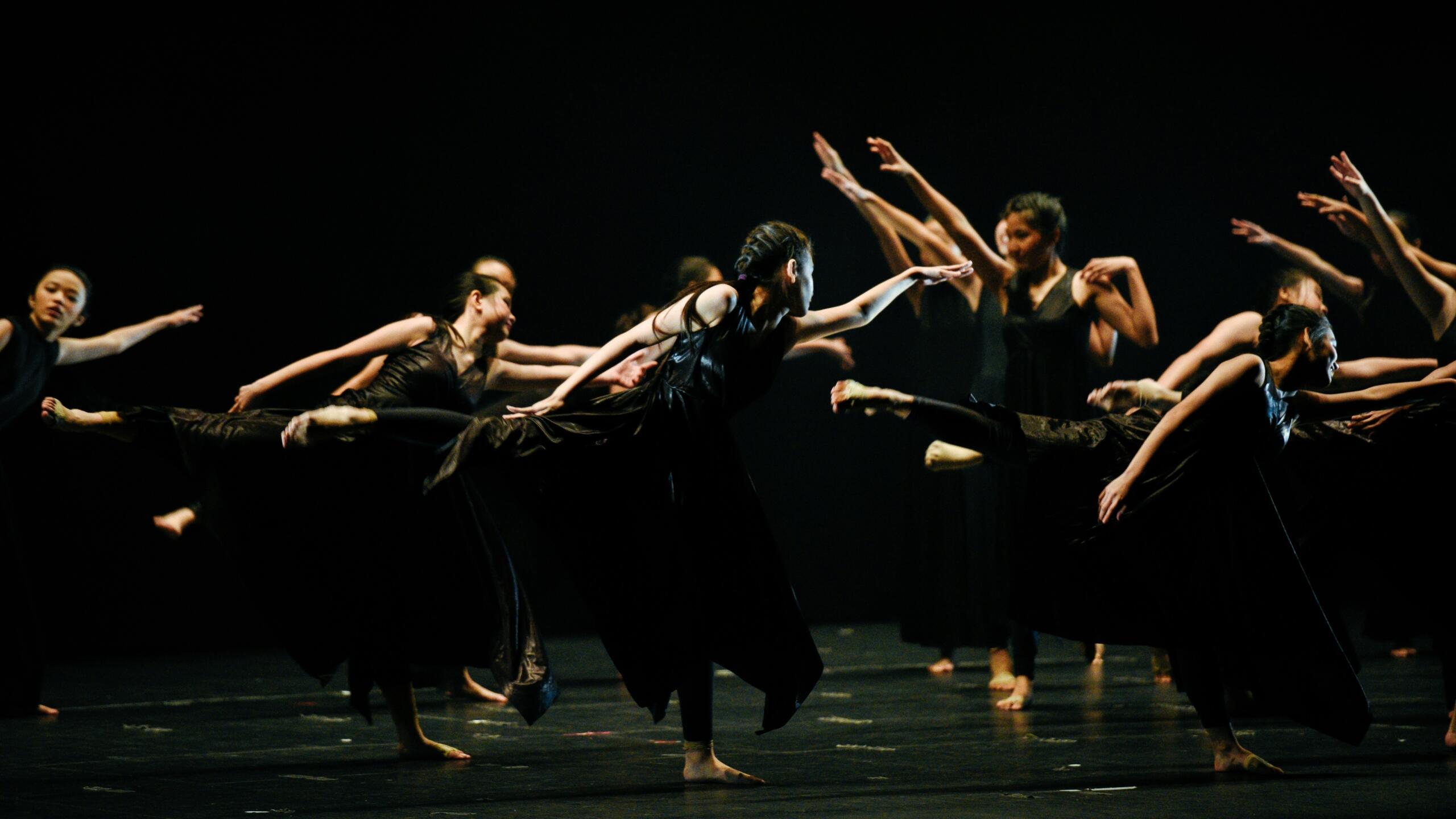 A group of dancers performs on a stage against a dark background.