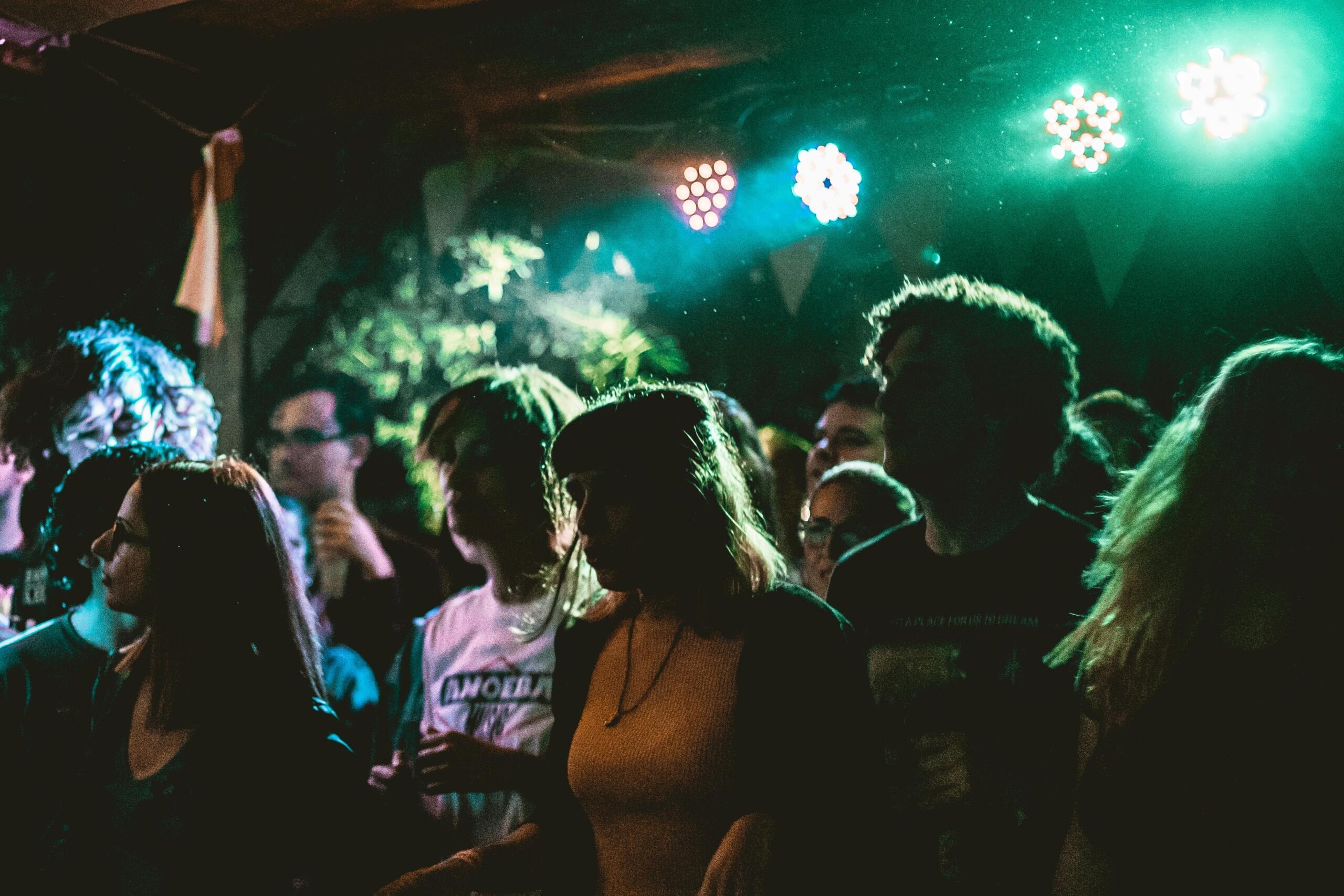 A crowd of people stands under colorful club lights.