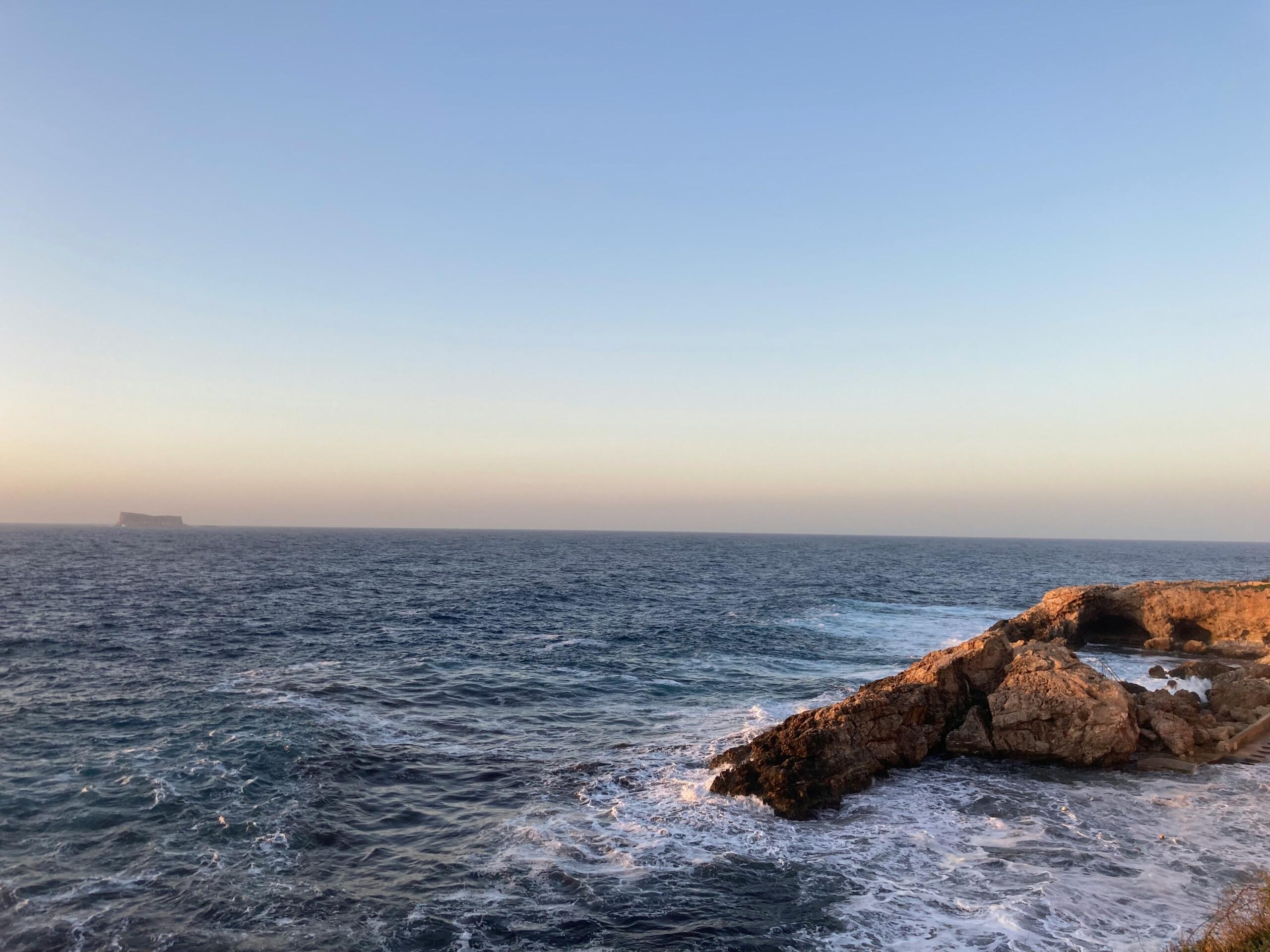 Malta limestone coastline meeting the open Mediterranean Sea at dusk with rocky foreshore.