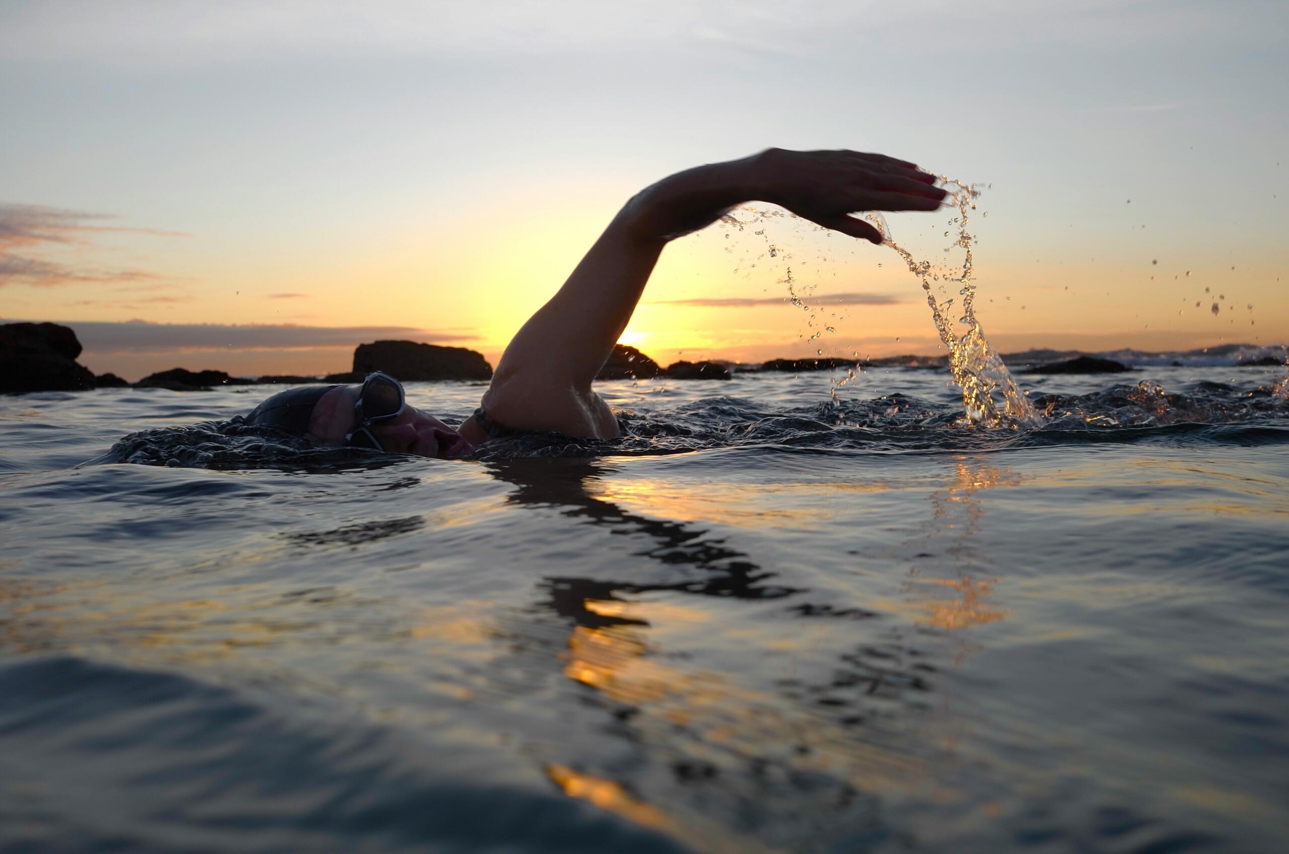 open water swimmer in the sea at sunset near rocky coastline