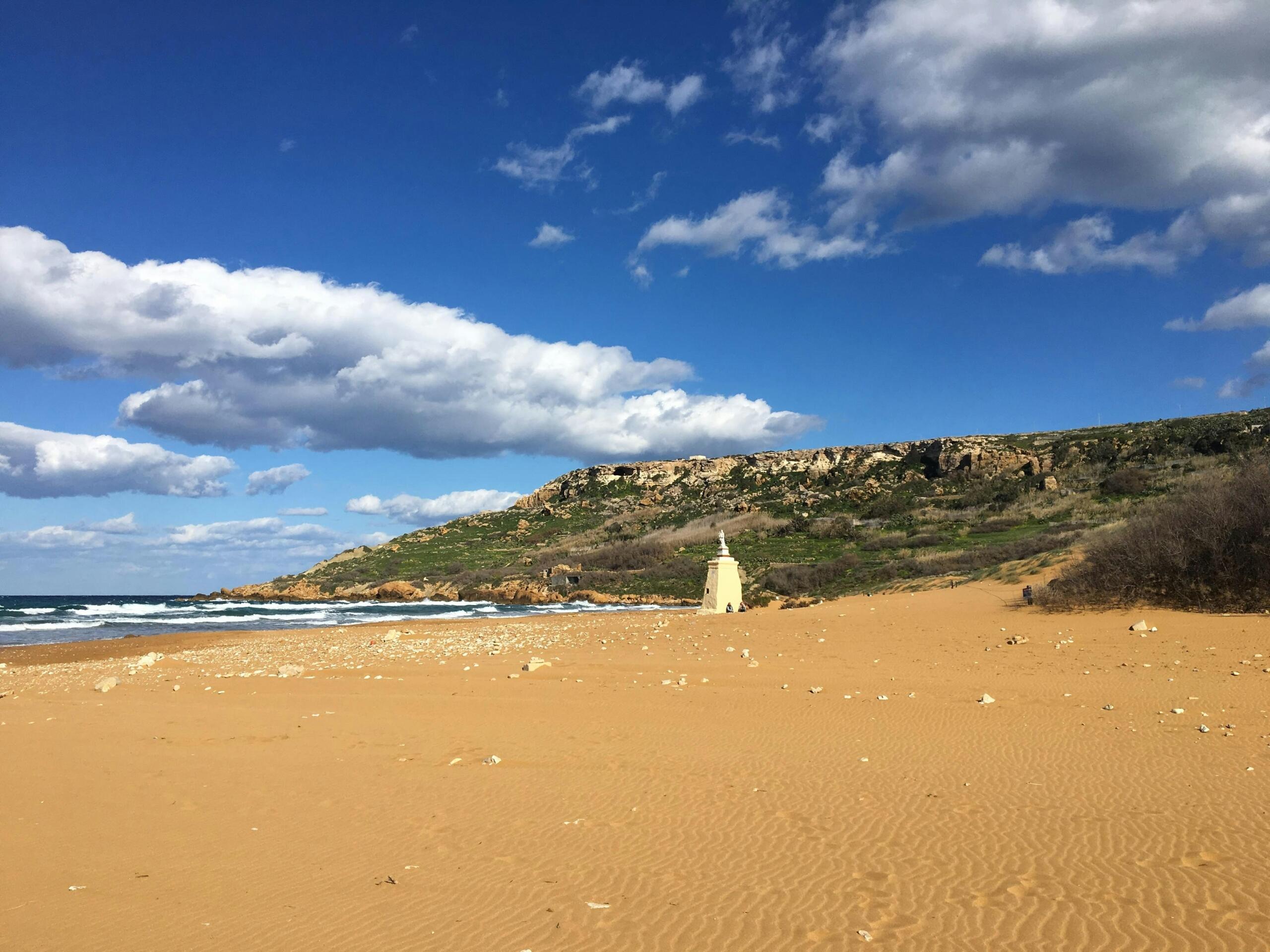 Empty red sand beach at Ramla Bay in Gozo with rocky cliffs and blue sky
