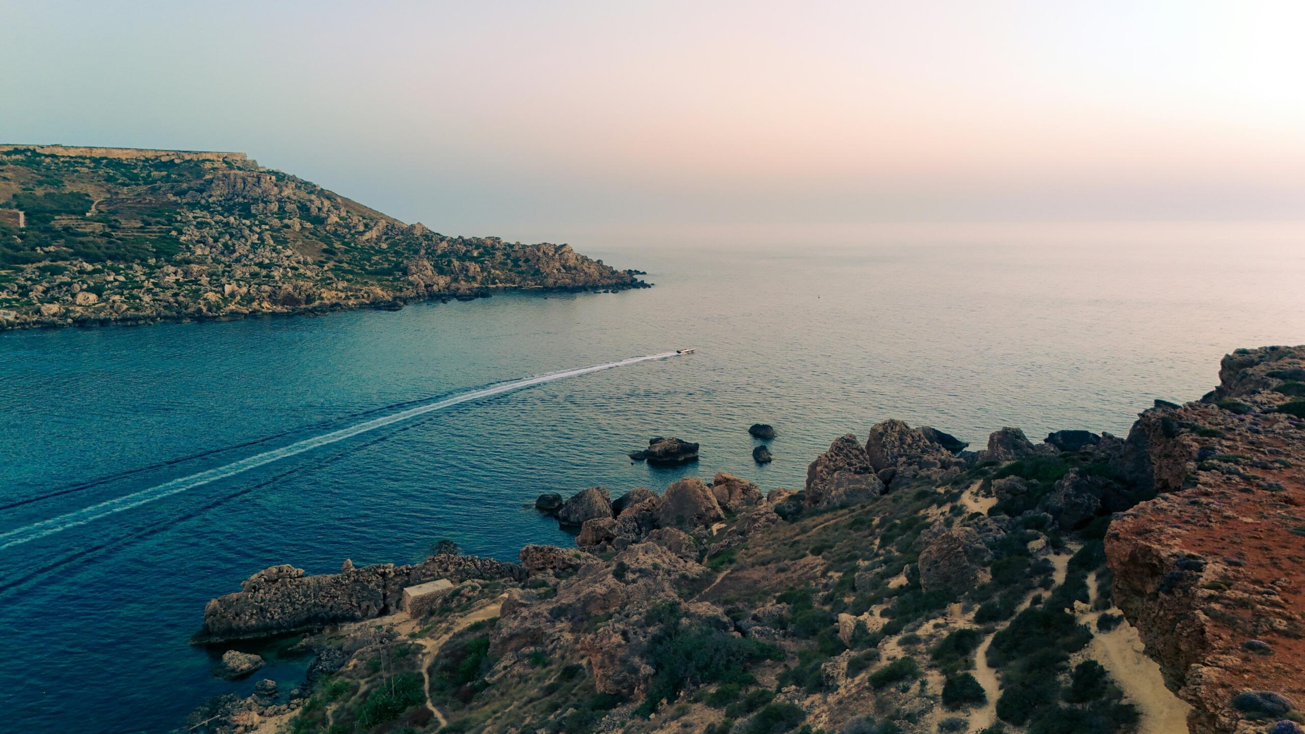 rocky Maltese coastline with calm bay and boat trail in the sea