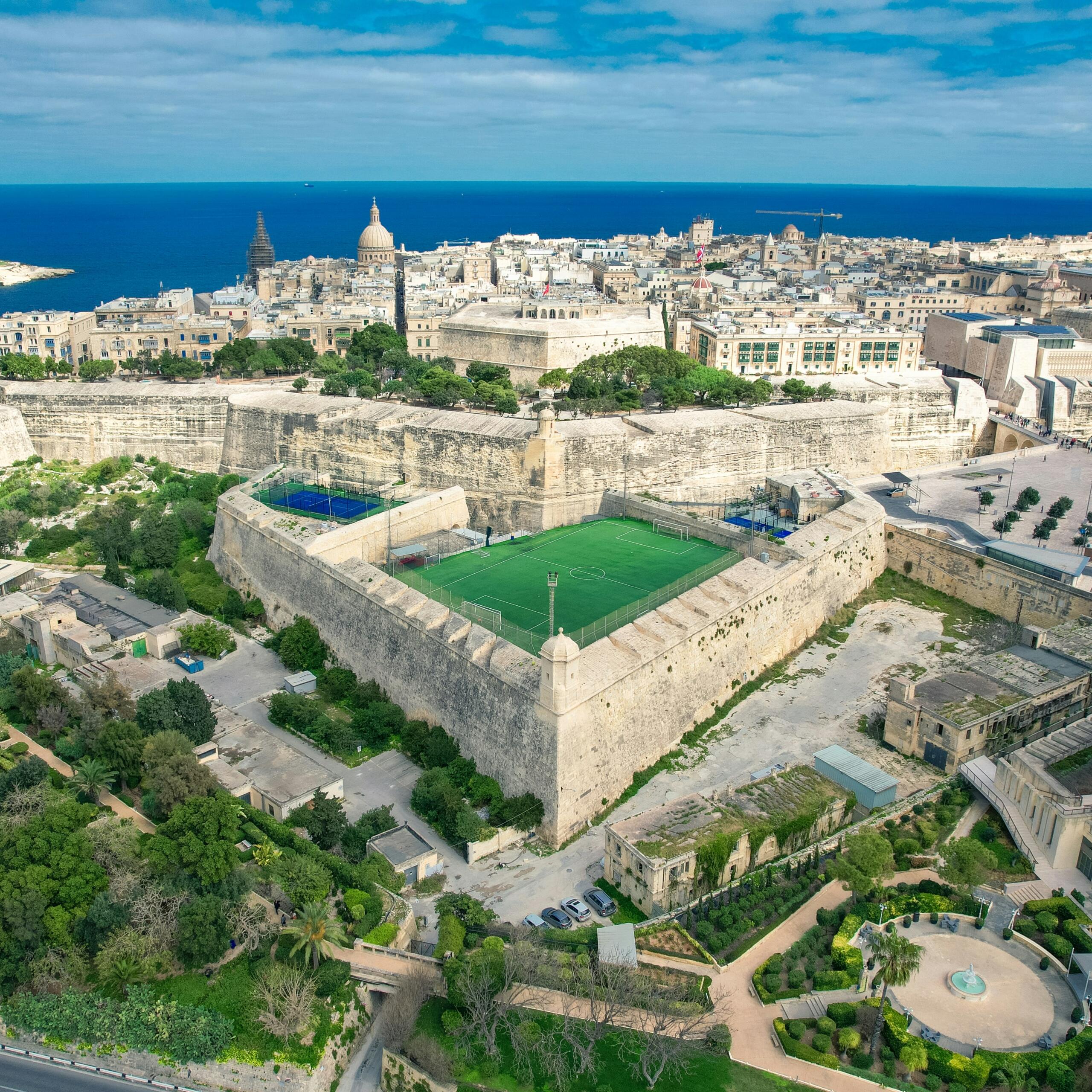 Aerial view of a football pitch set within the historic bastions of Valletta Malta with the Mediterranean Sea in the background.