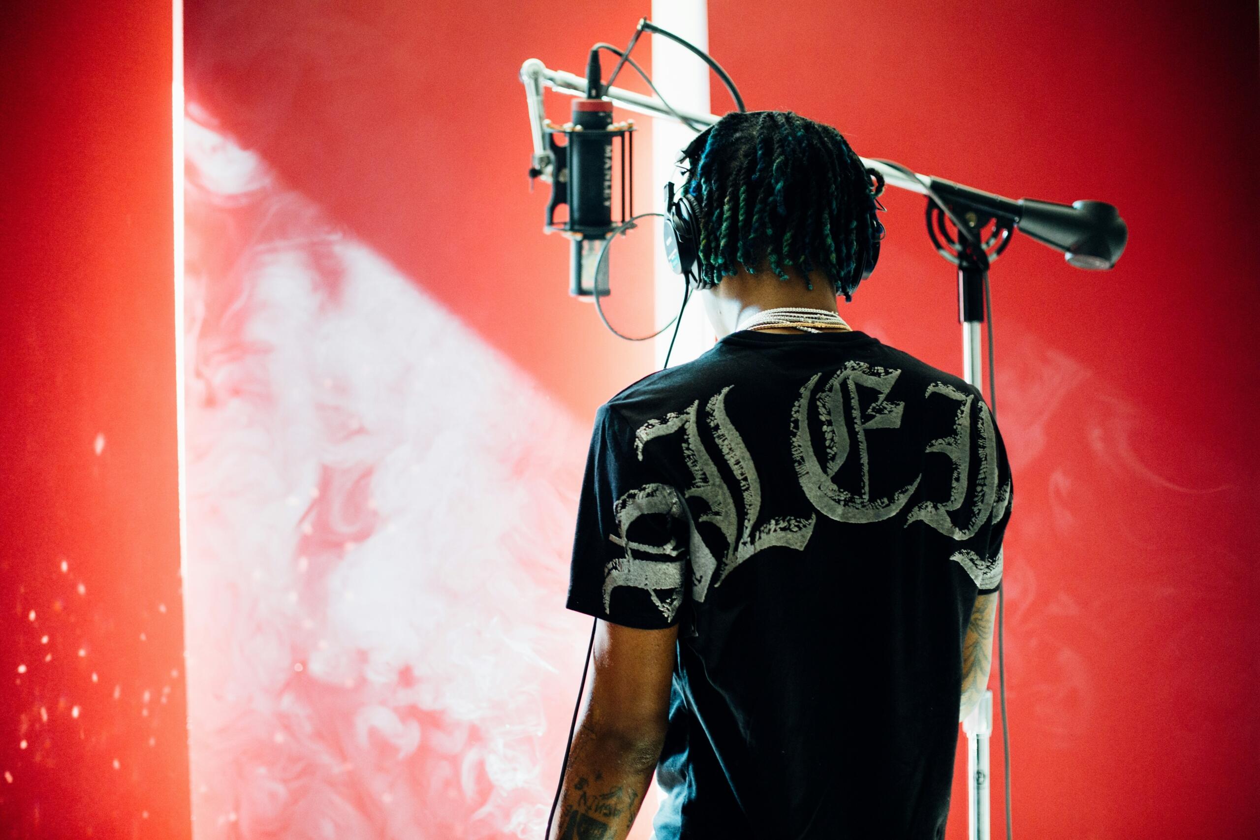 A man stands in front of a condenser microphone in a recording studio.
