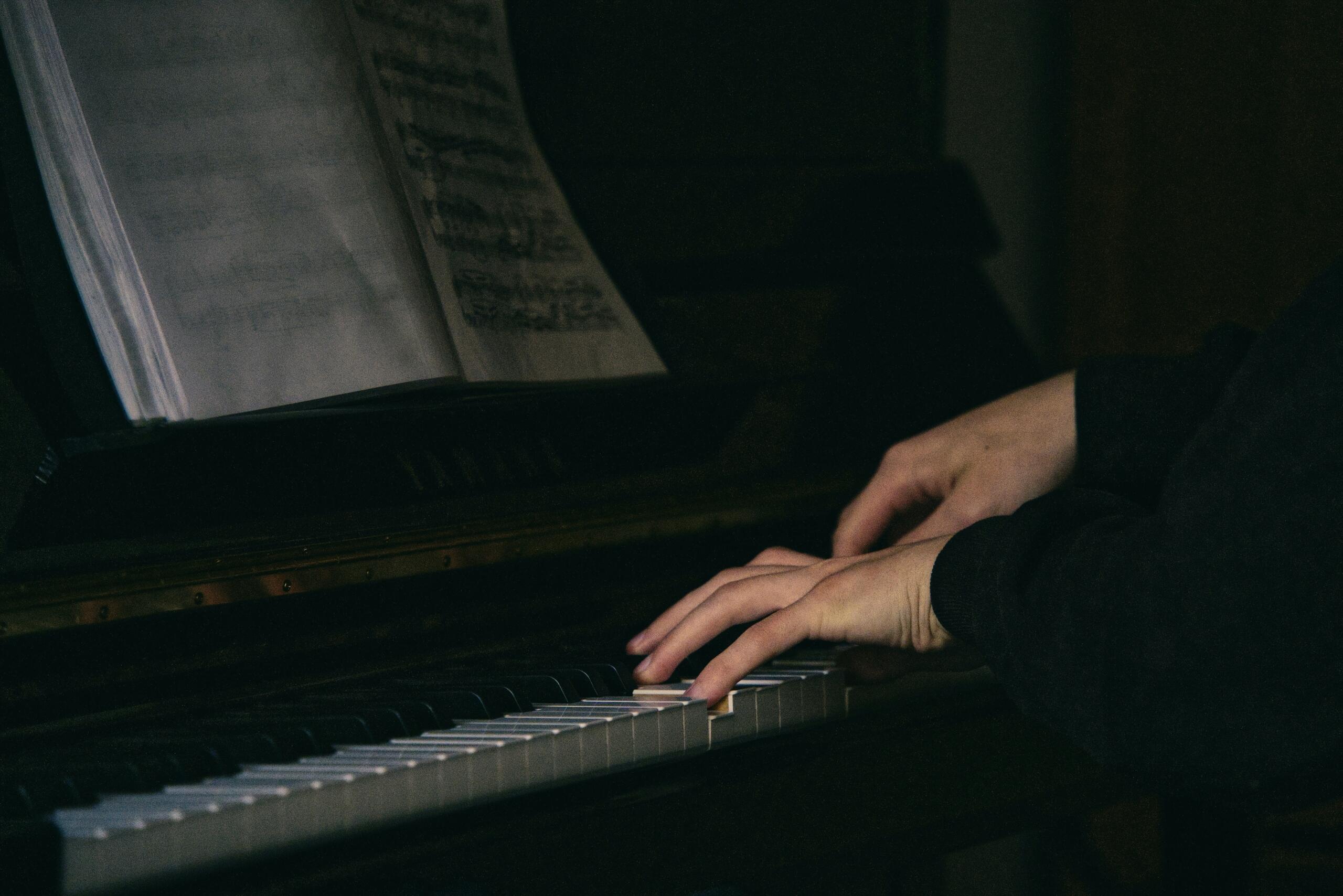 Two hands play a piano with open sheet music above the keyboard.