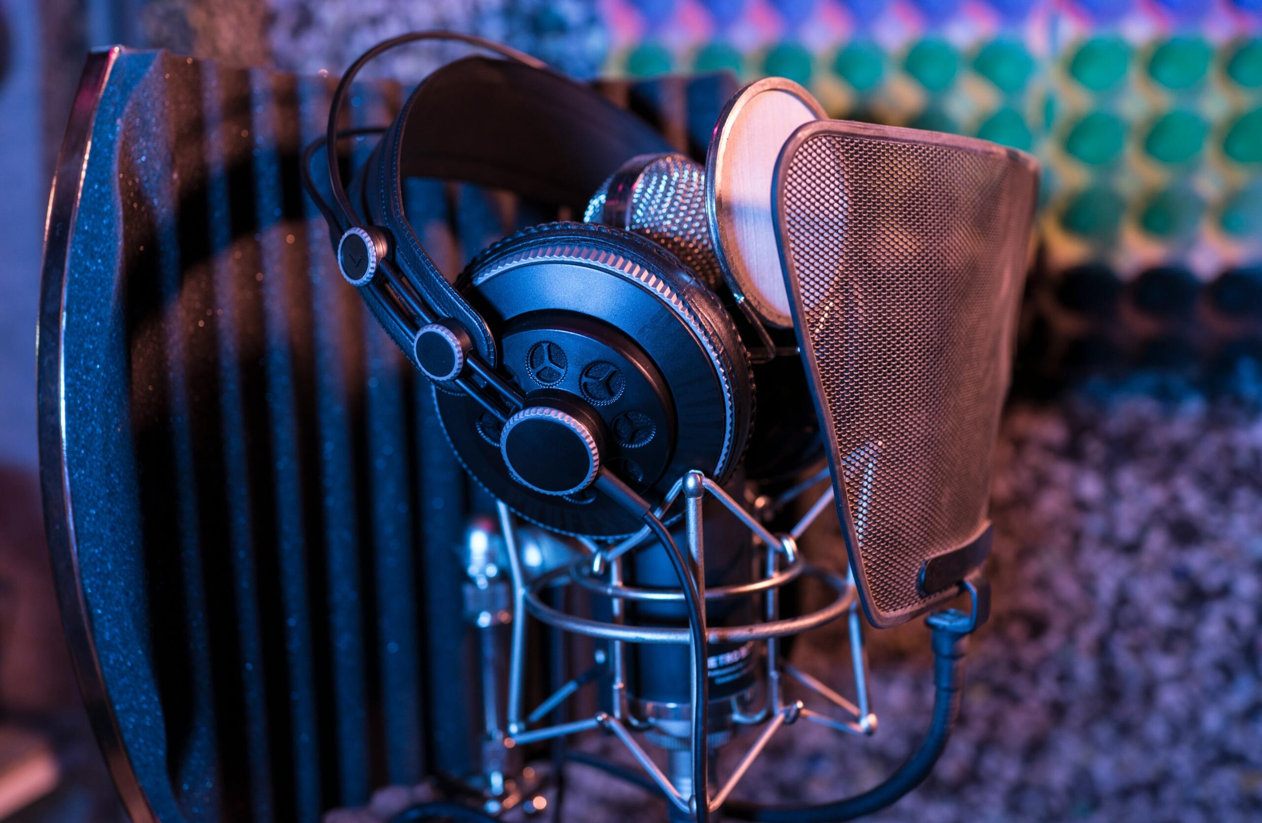 Headphones rest against a studio microphone fitted with a pop filter.