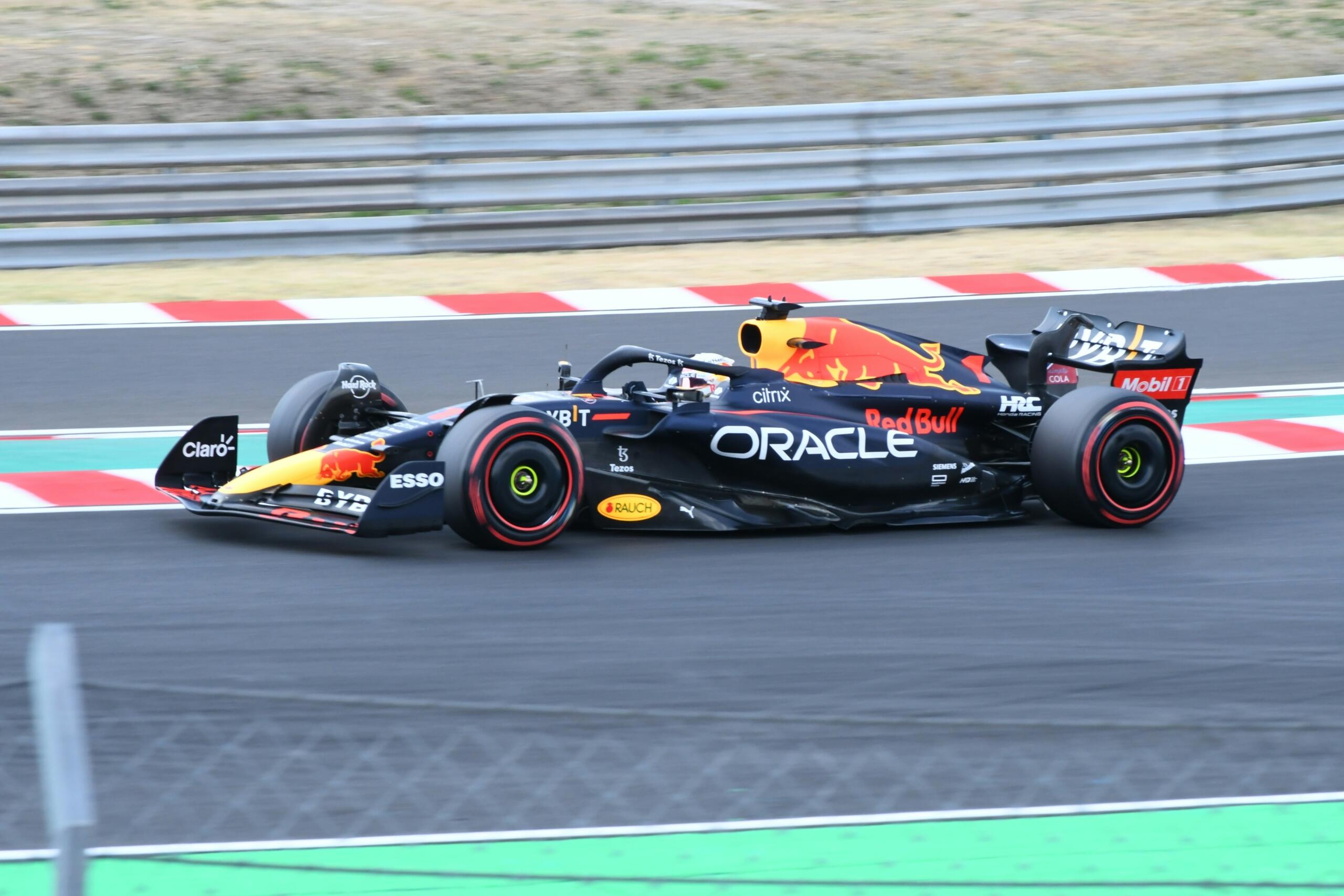 A side view of an Oracle Red Bull Racing Formula 1 car racing around a circuit, with red-and-white kerbs and safety barriers visible in the background