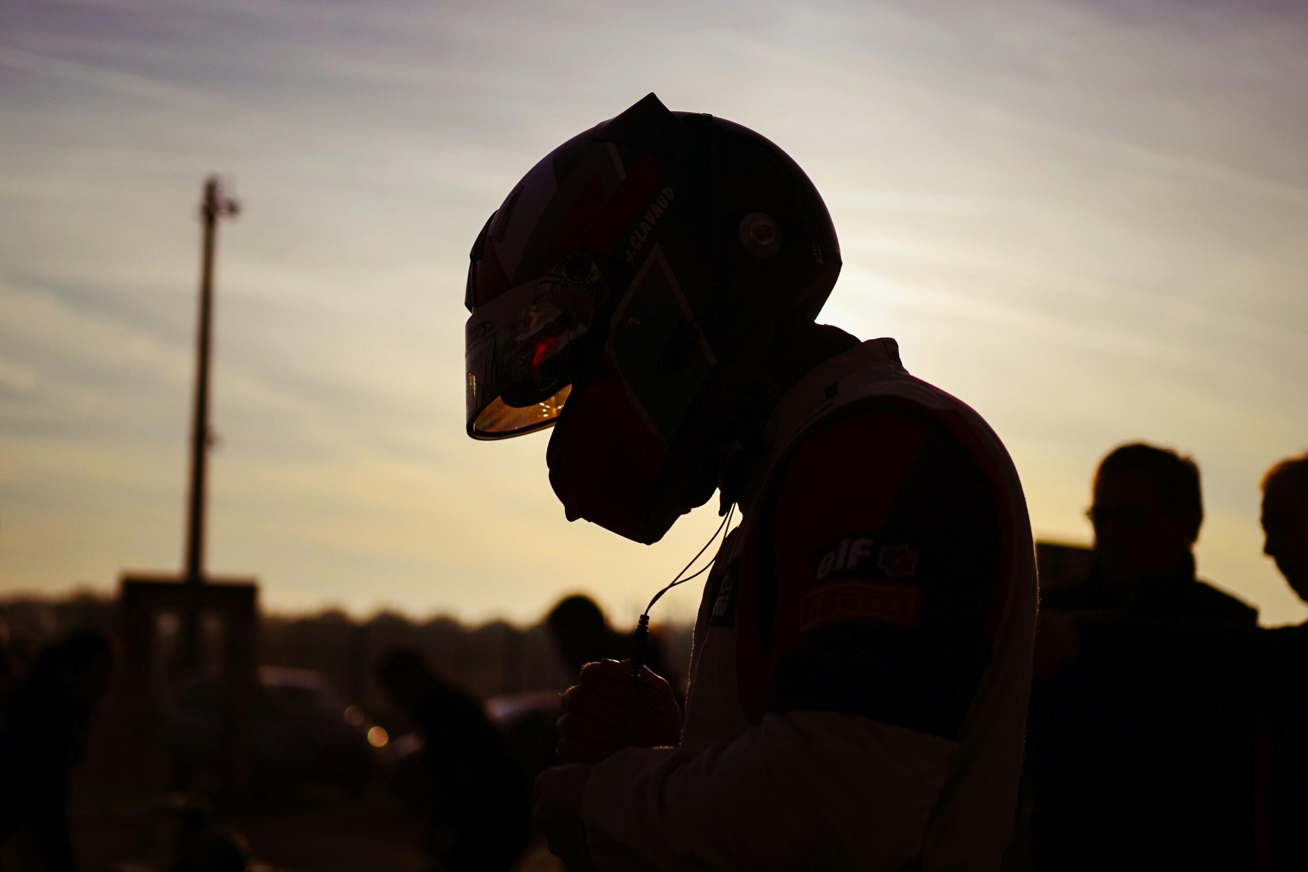 Silhouette of a Formula 1 driver wearing a racing helmet at sunset near the paddock.