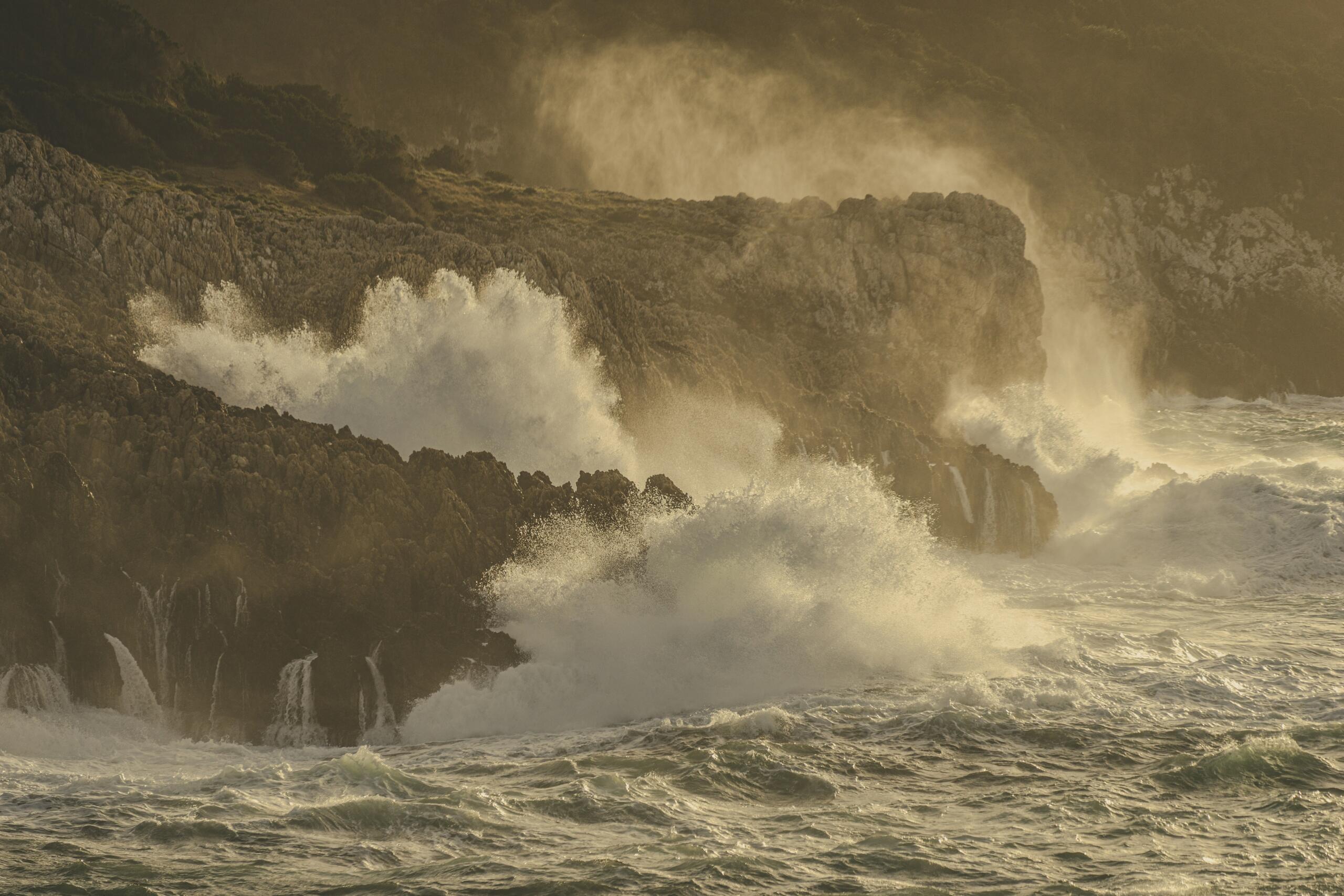 Powerful waves crashing against a rocky coastline in warm golden light