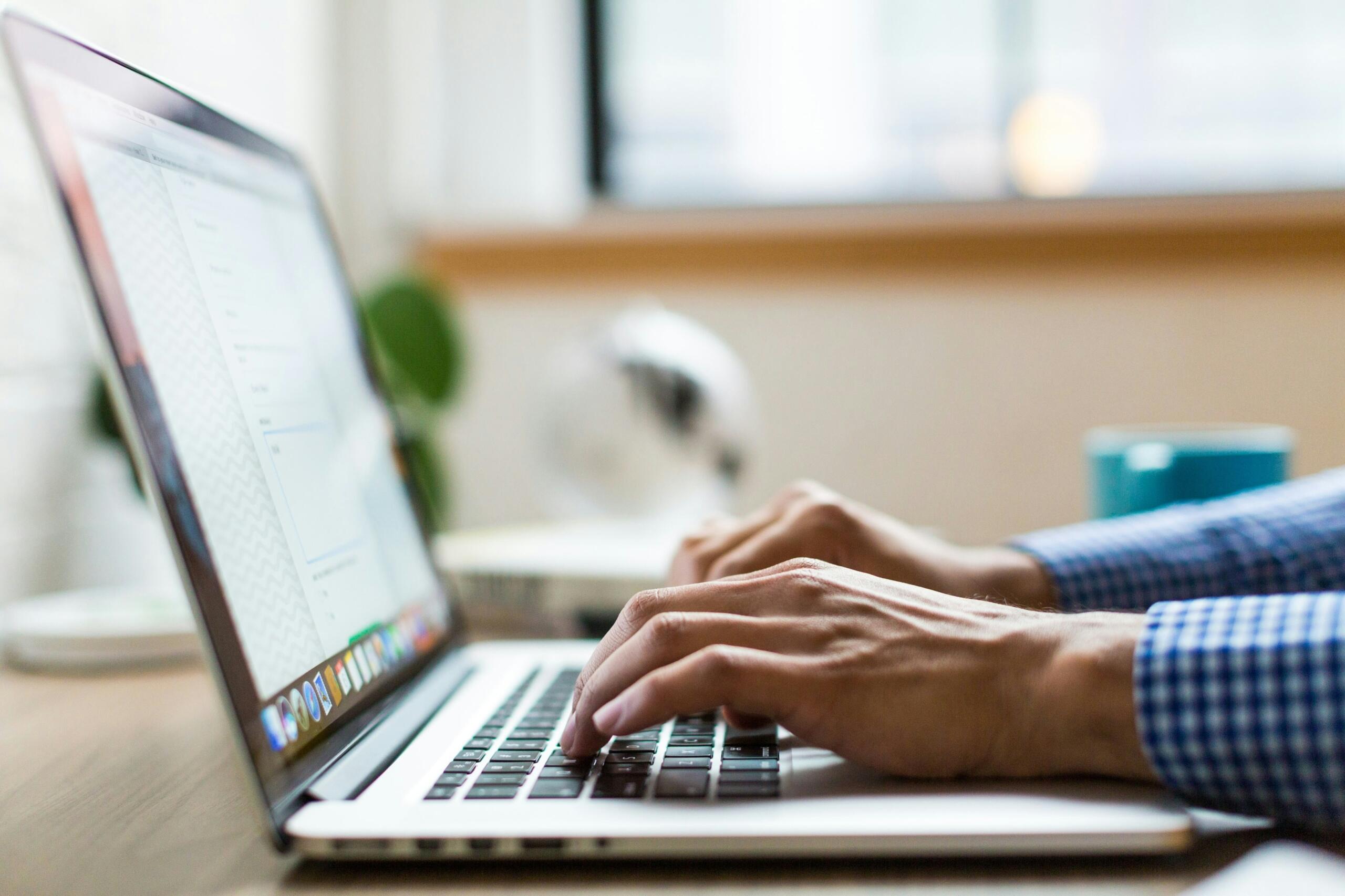 Close-up of hands typing on a laptop, checking information on screen
