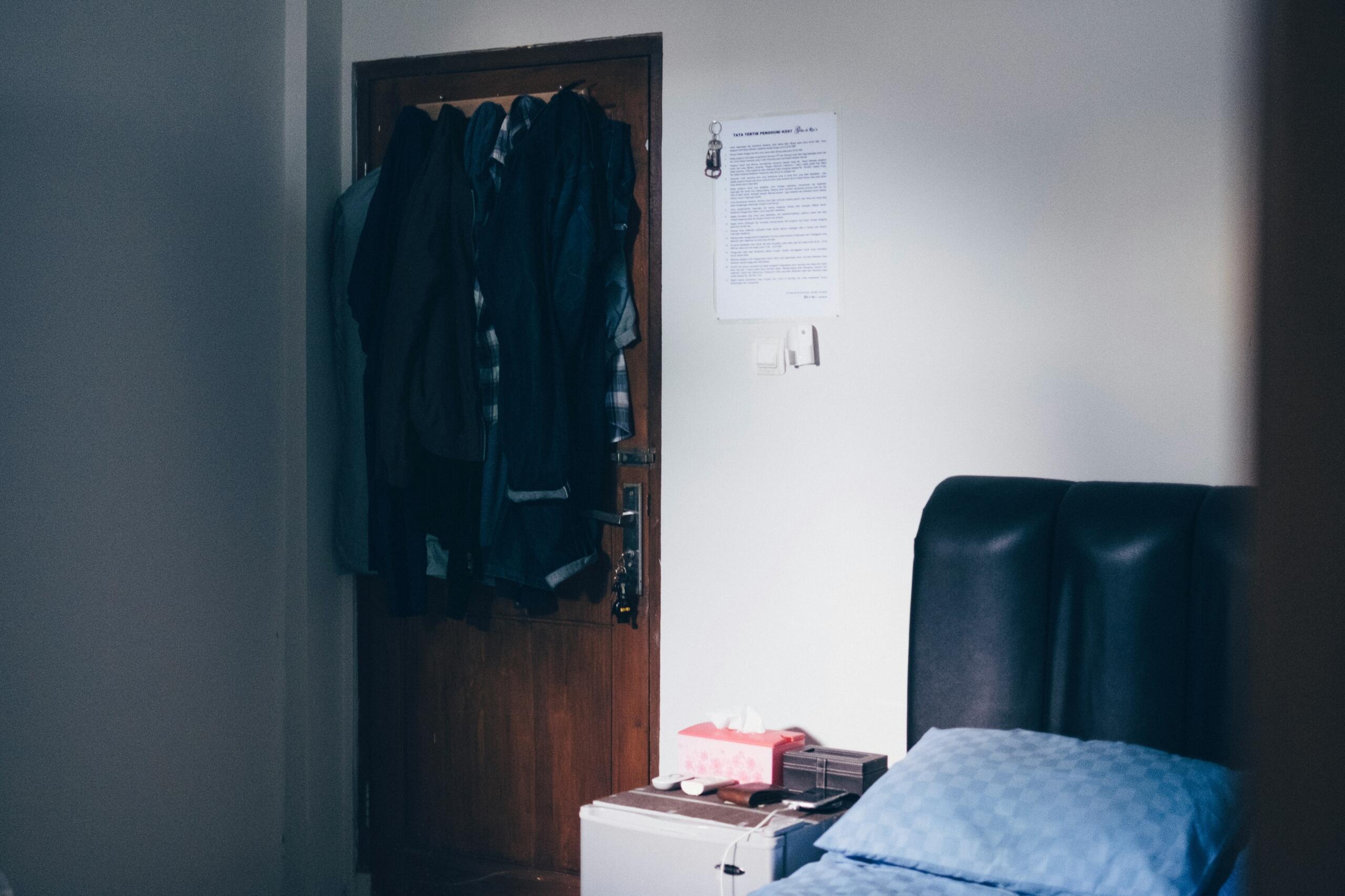 Simple shared student room with bed and clothes hanging on door