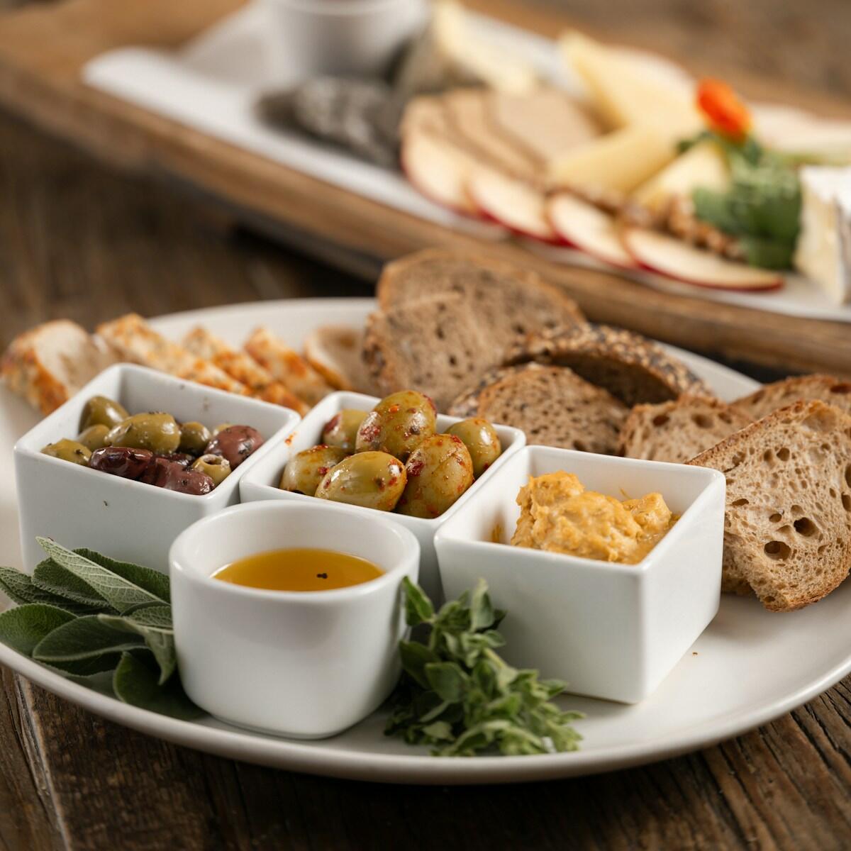 A platter of bread, olives, olive oil and savoury dips on a wooden table.