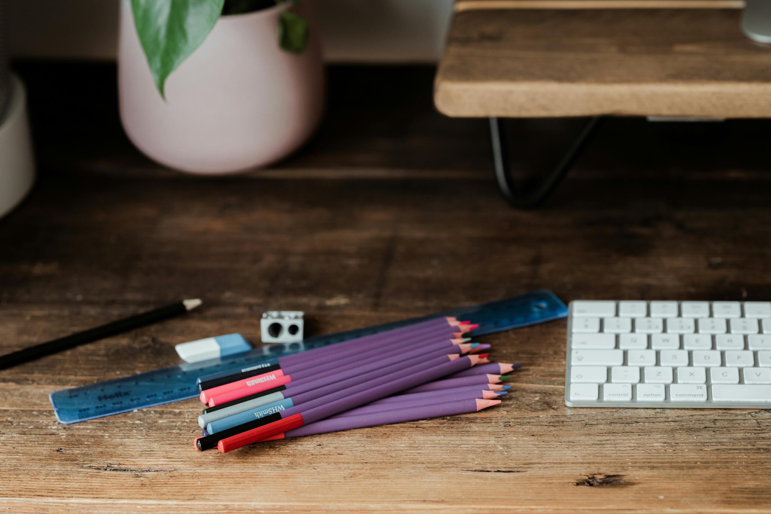 Coloured pencils, a ruler, an eraser and a sharpener on a wooden desk beside a keyboard