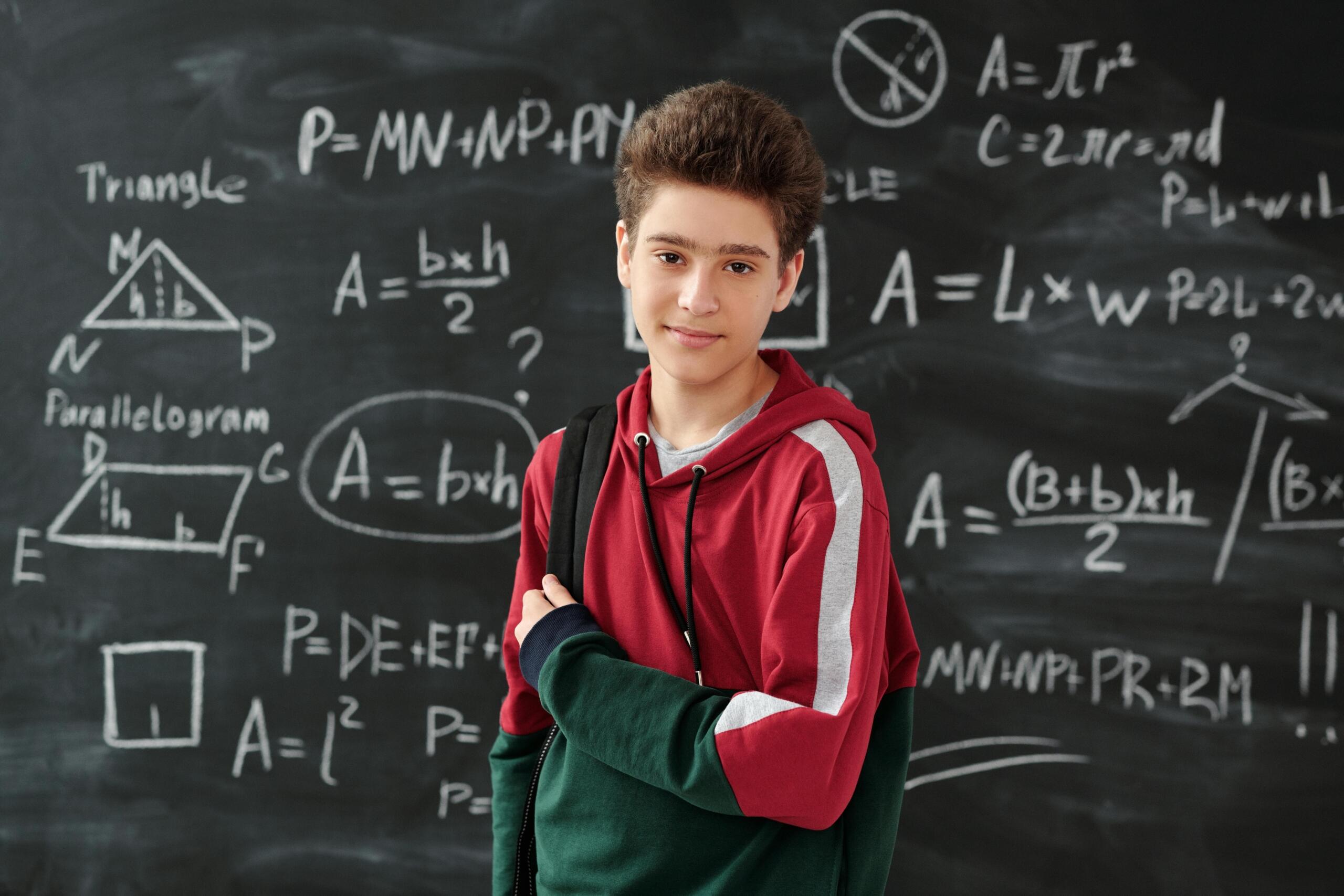 Boy in red hoodie standing in front of blackboard