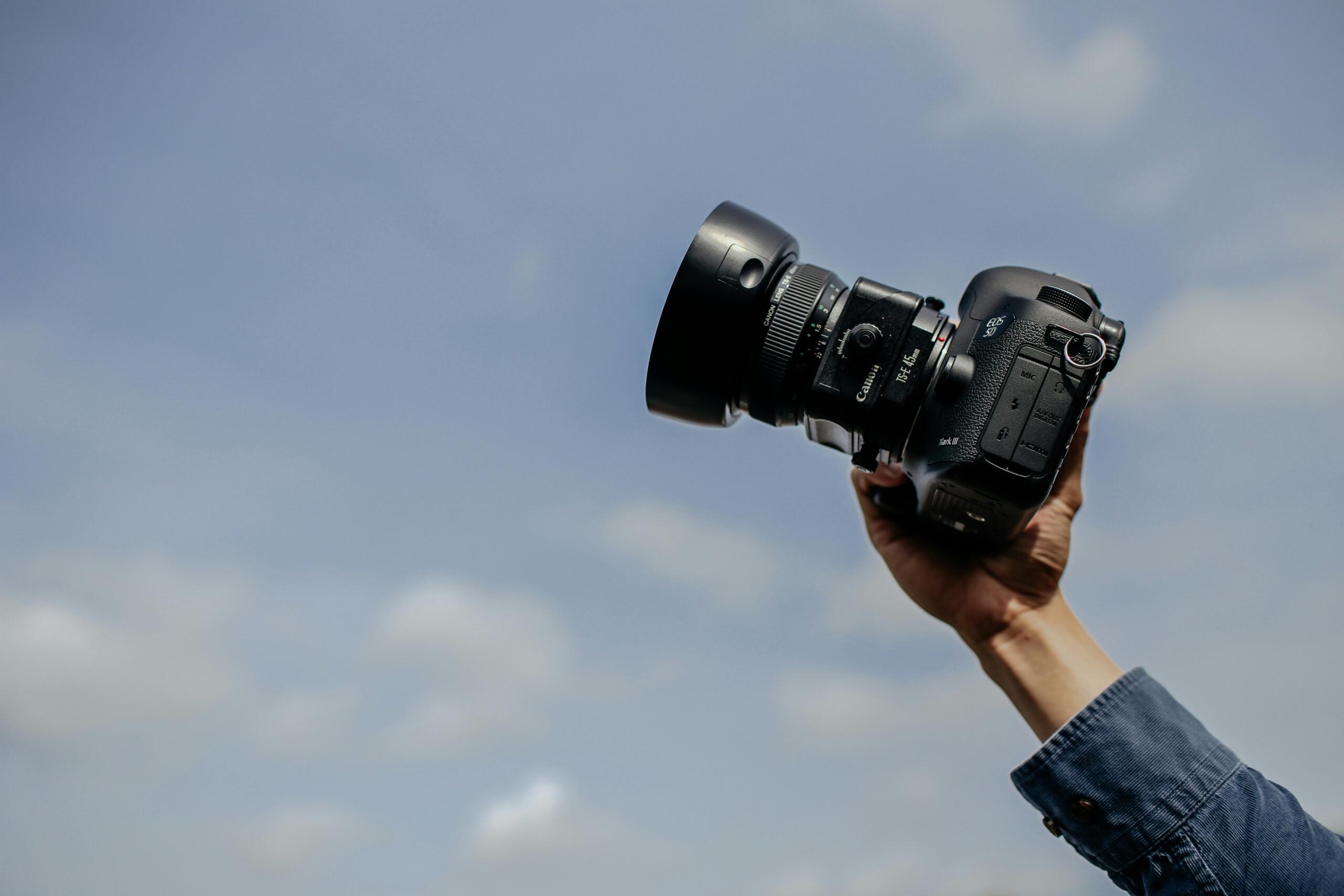 A person's hand holding a camera to the sky.