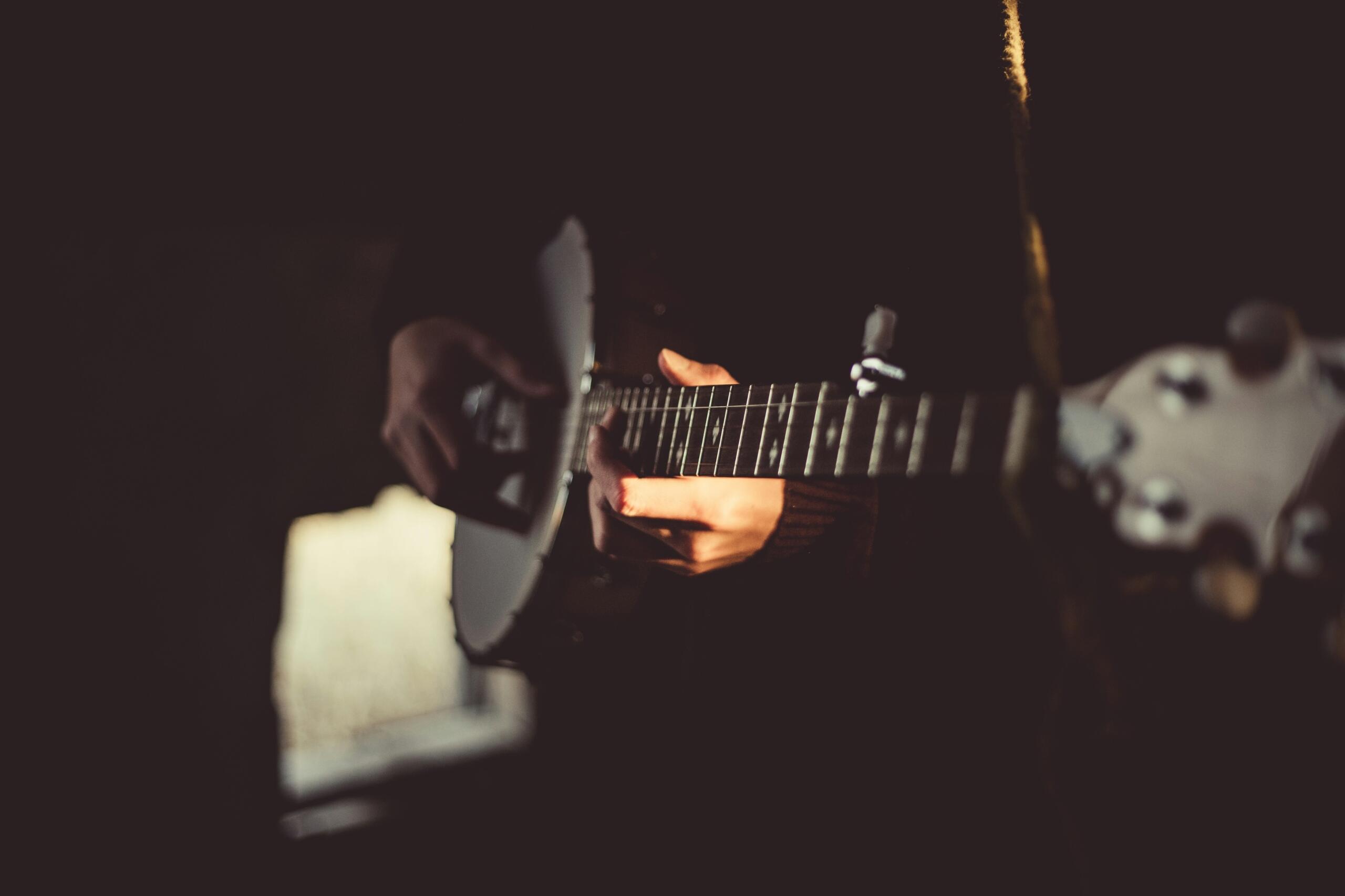 Close-up of a person playing a banjo, with warm light illuminating their hands and instrument against a dark background.
