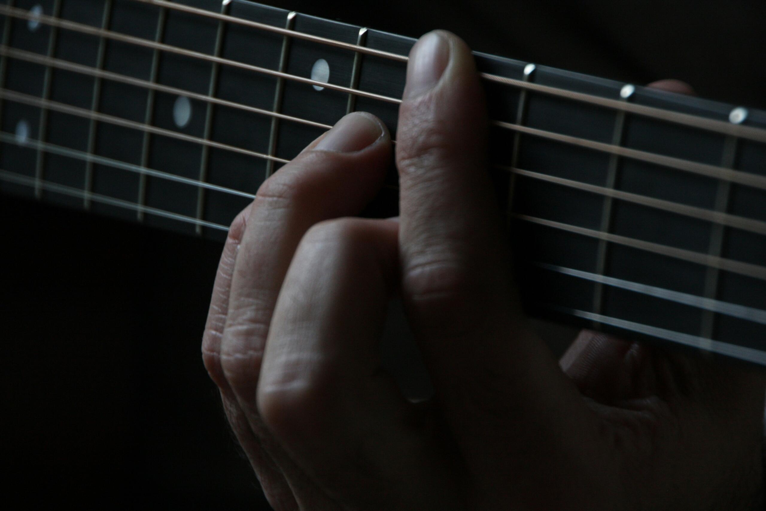 A close-up view of a person’s hand pressing down guitar strings on the fretboard.