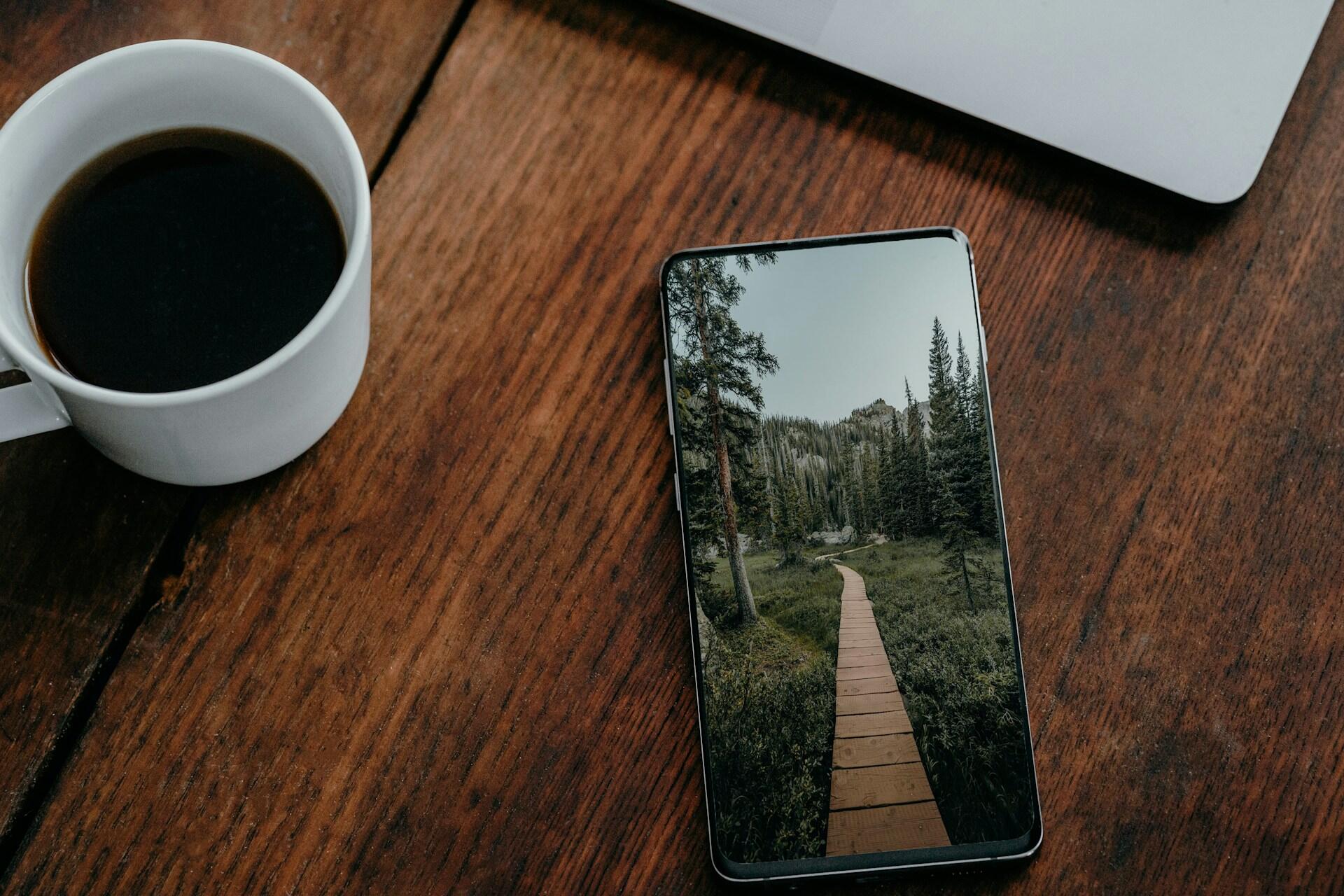 A smartphone lying next to a cup of coffee on a wooden table