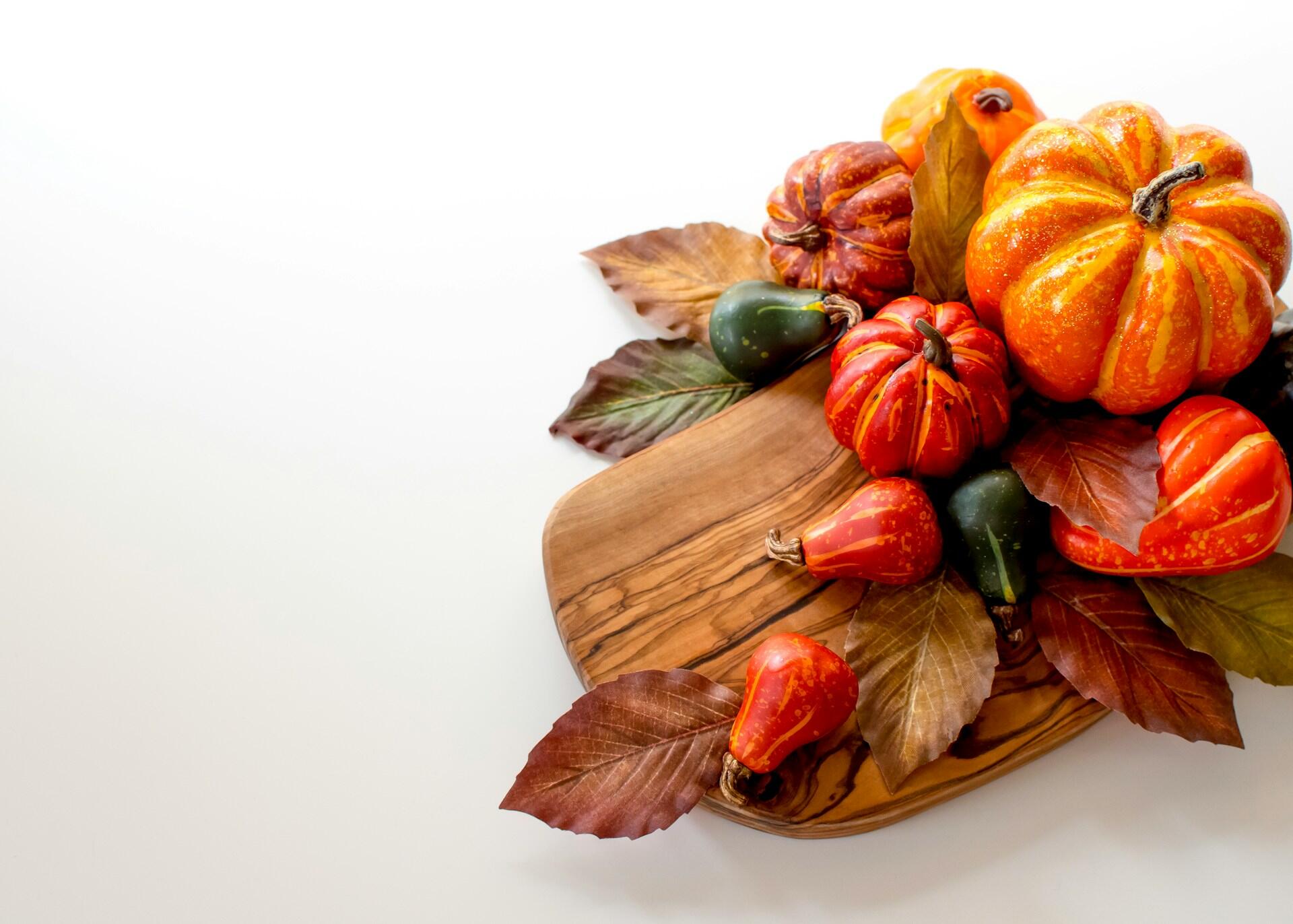 Orange and green gourds and leaves arranged on a brown wooden chopping board