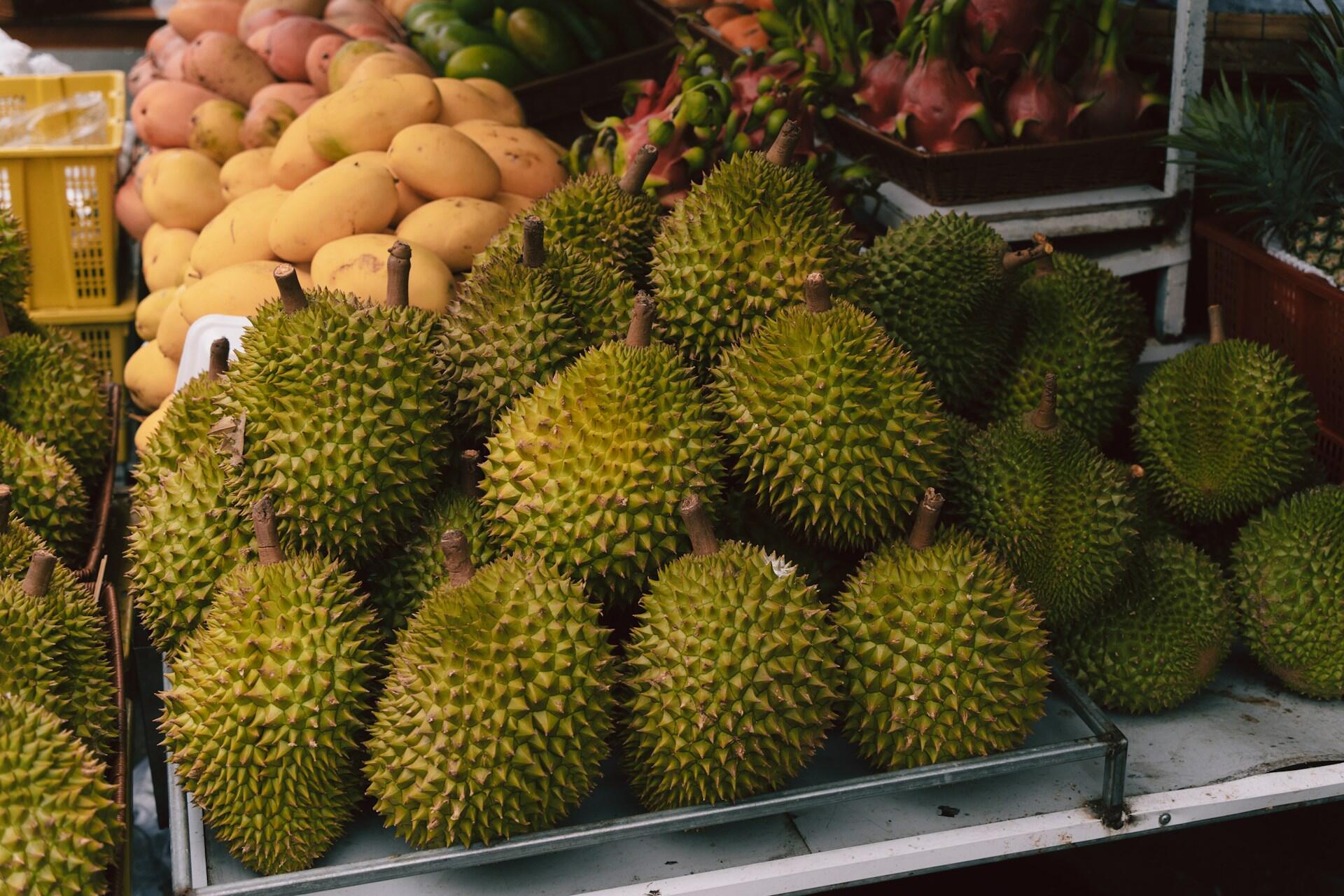 Durian, mangoes, dragon fruit, and pineapples piled up at a fruit stall in a Southeast Asian market