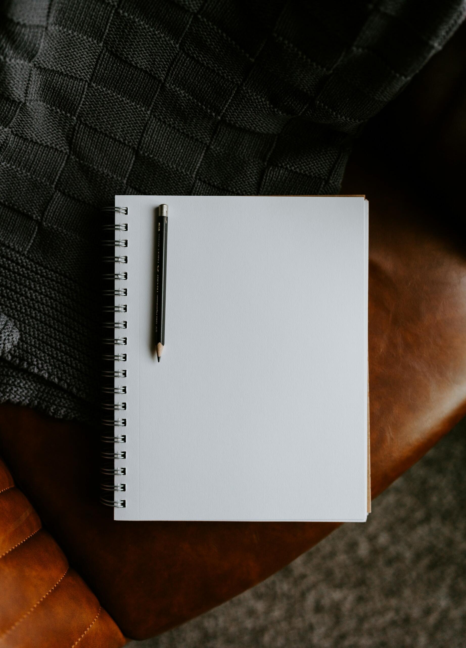 A plain spiral-bound sketchbook with a pencil resting on its blank page