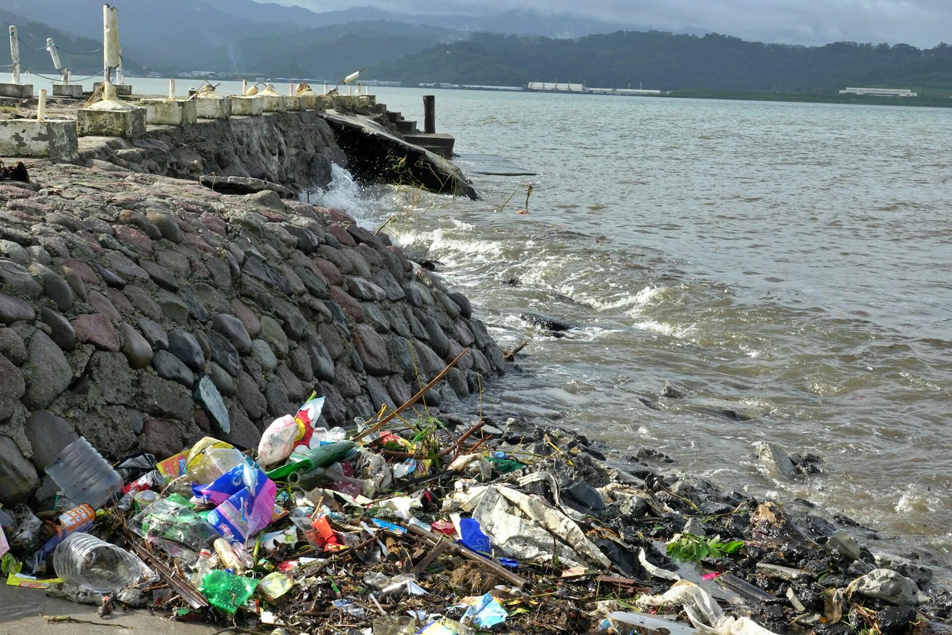 Piles of plastic waste scattered along a seashore beside a stone wall.