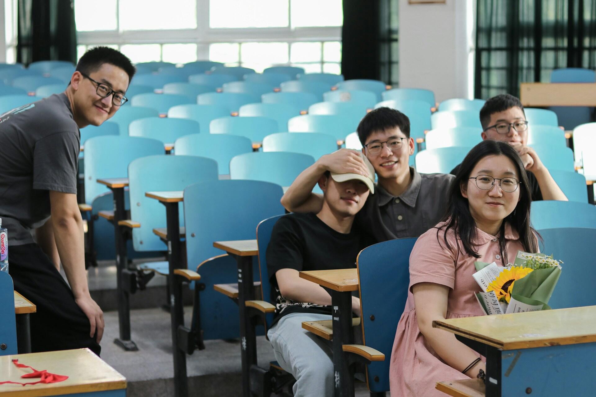 A group of men and a woman sitting on classroom chairs and posing for a picture
