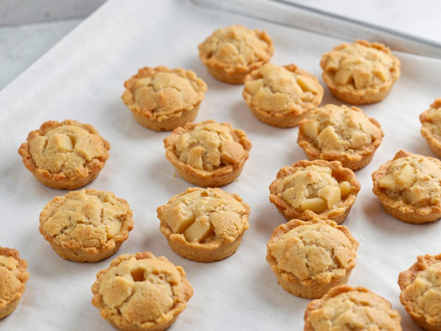 Rows of freshly baked vegan apple pie bites on a parchment-lined baking tray.